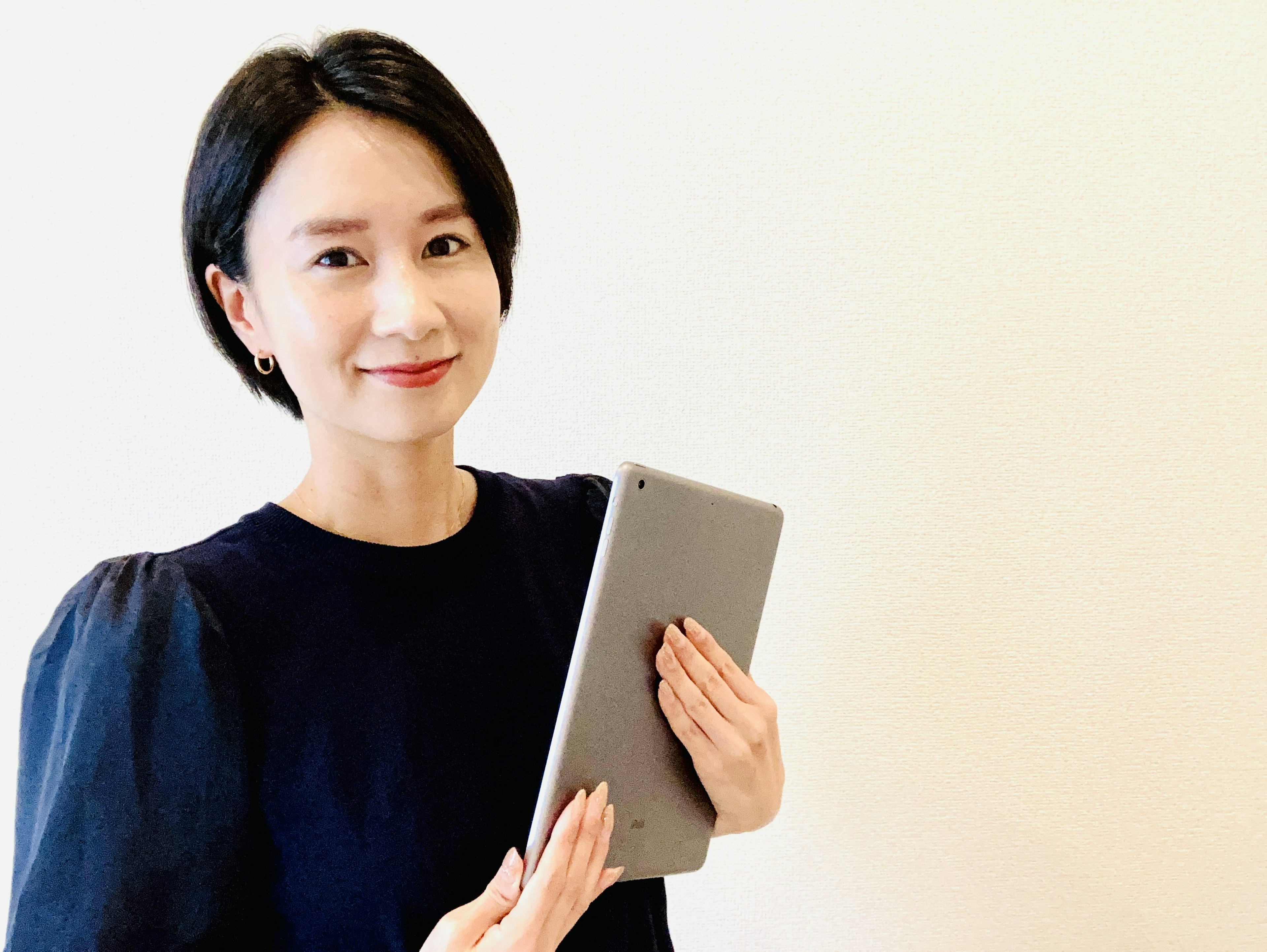 Woman smiling while holding a tablet against a simple background