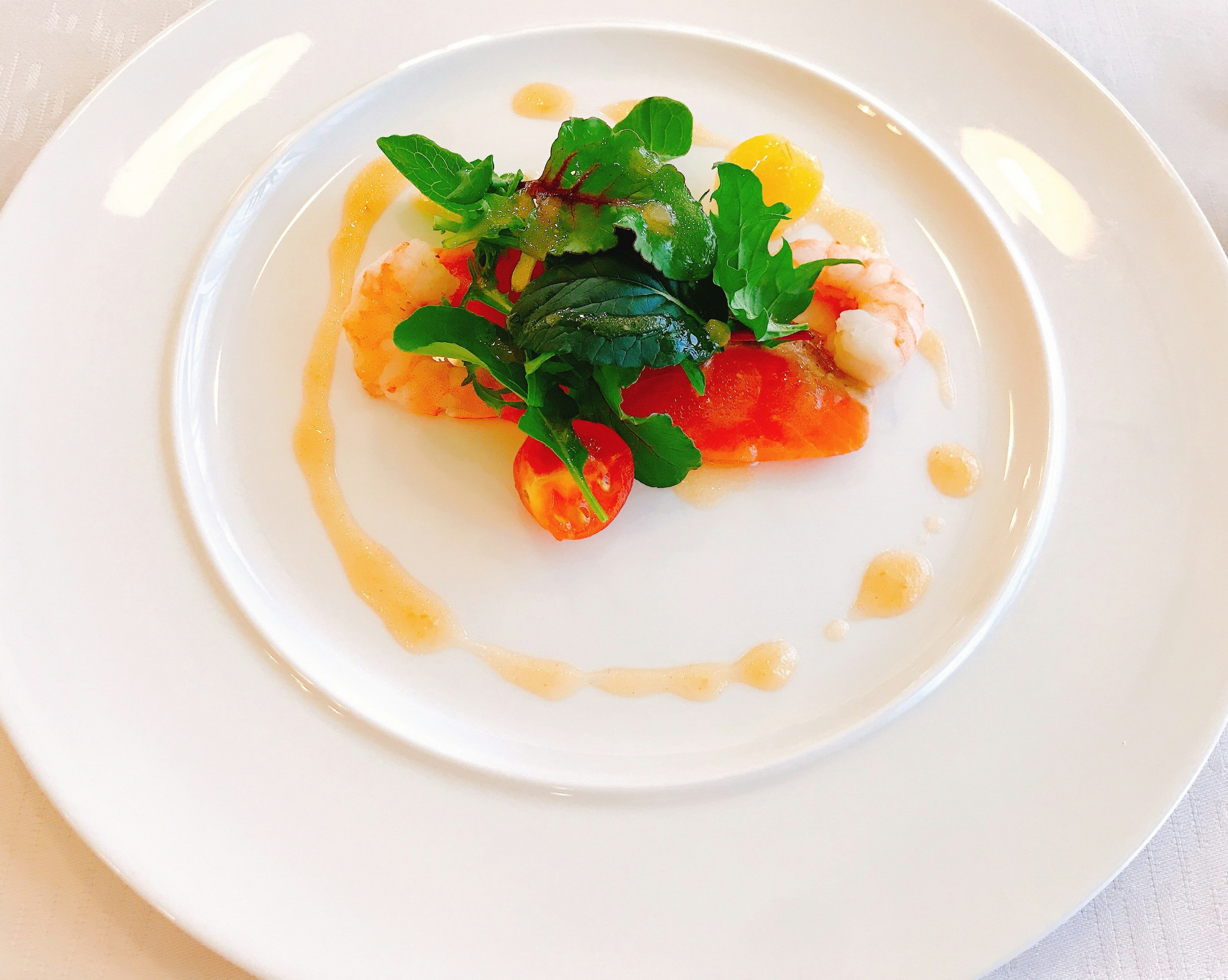 Un plato de mariscos bellamente presentado en un plato blanco, cubierto con tomates frescos y hierbas