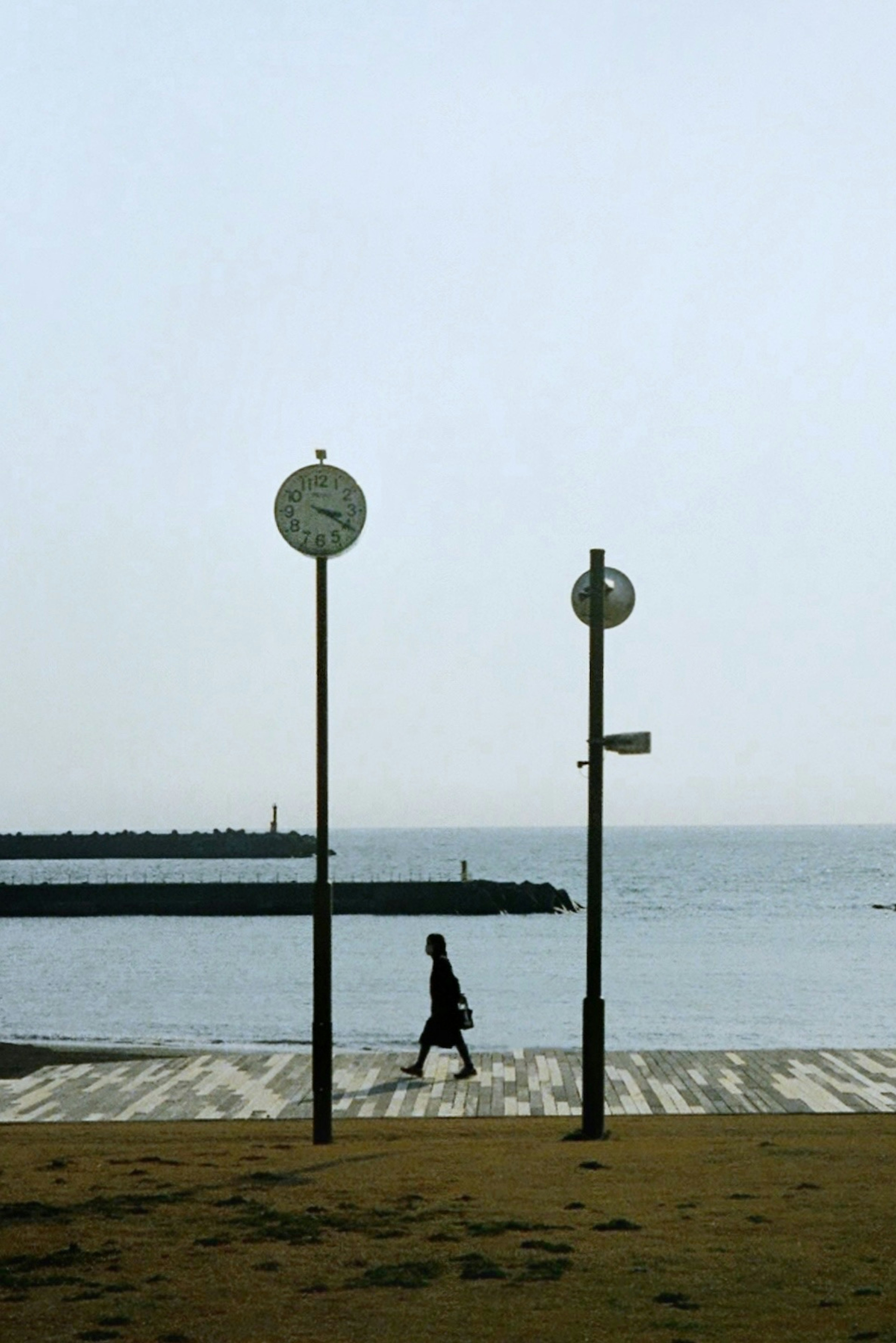 A person walking along a seaside promenade with clocks