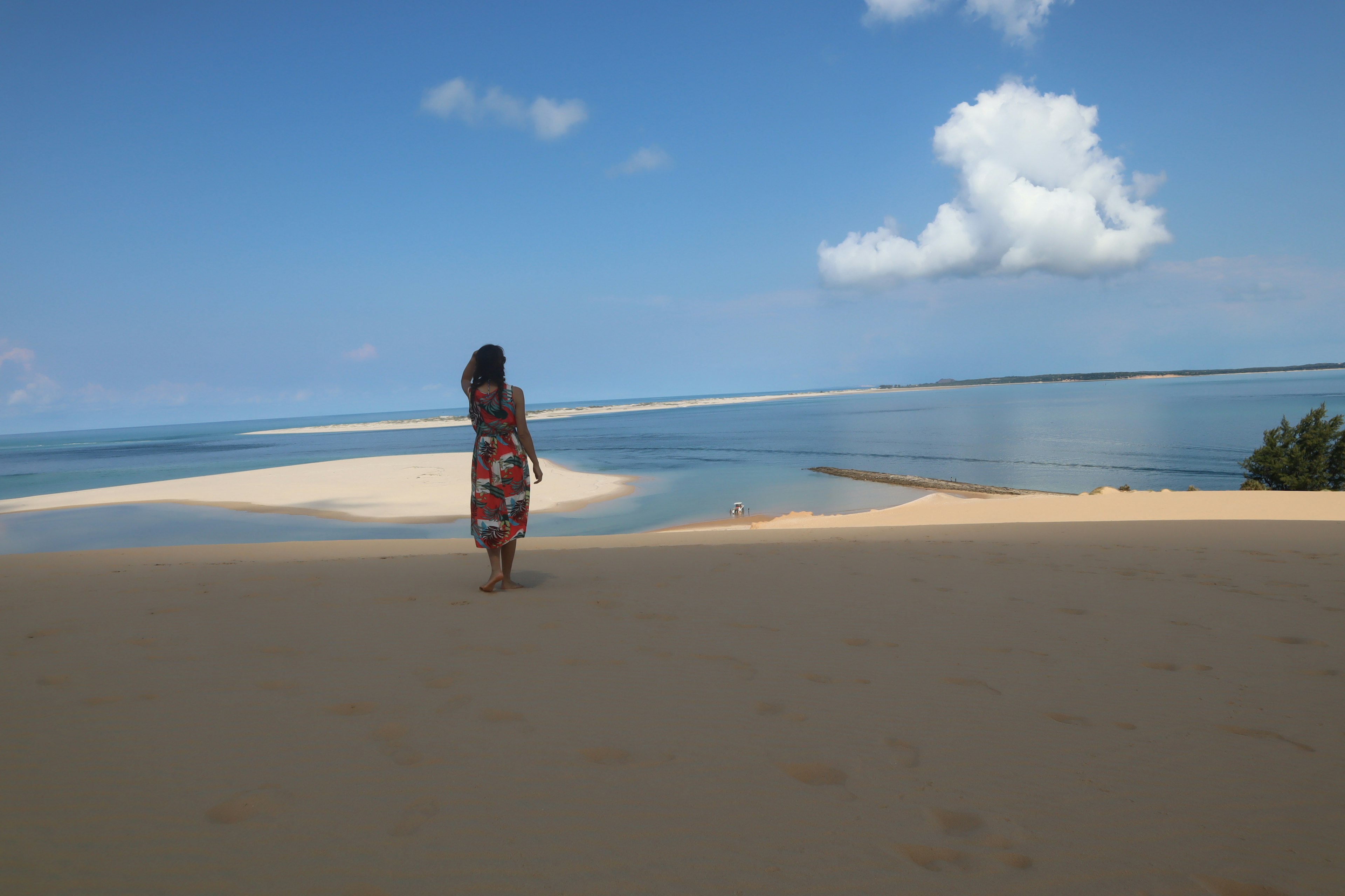 Une femme marchant sur une plage de sable avec la mer et le ciel bleus