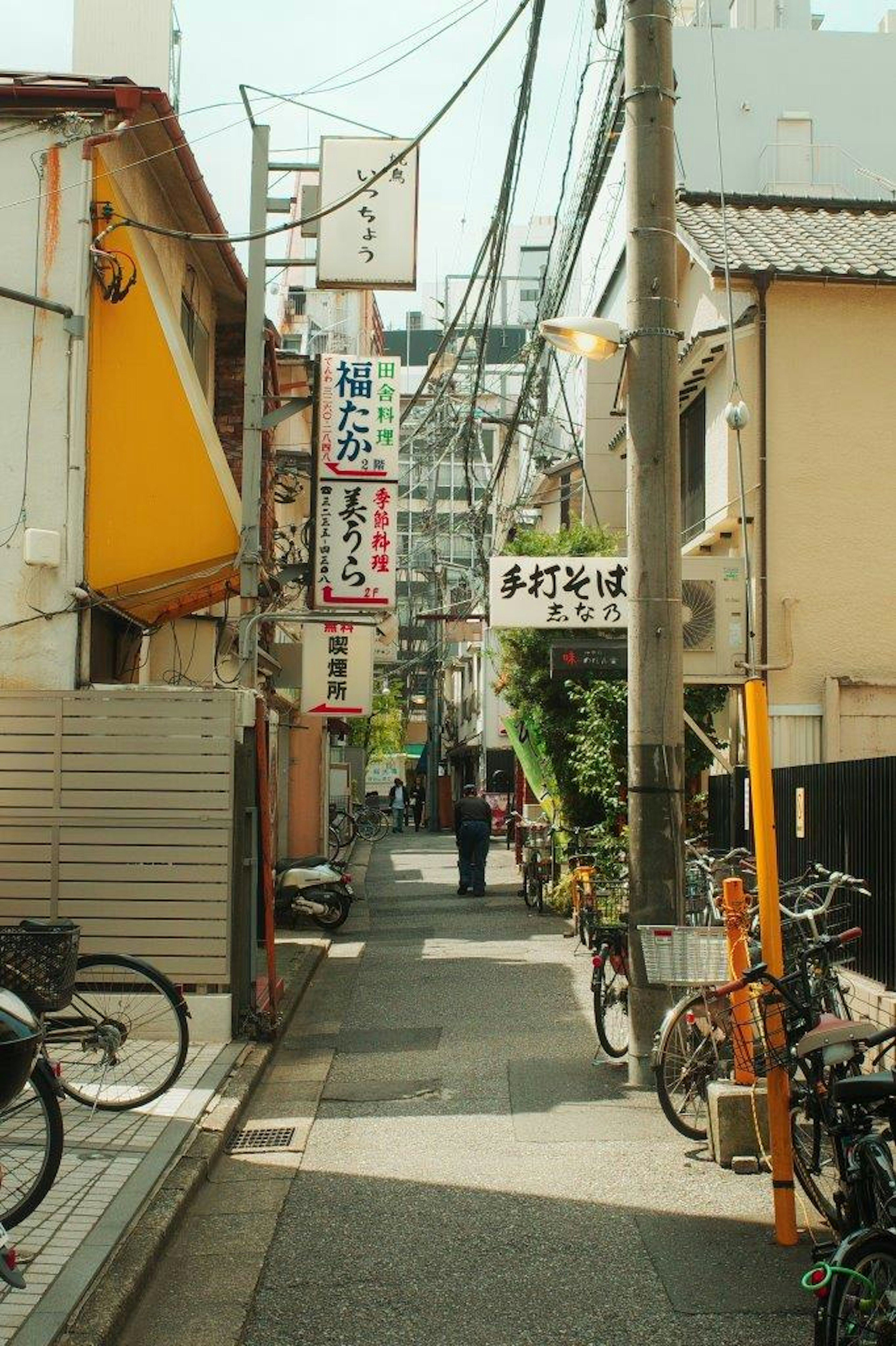 狭い路地に並ぶ飲食店の看板と自転車が見える風景