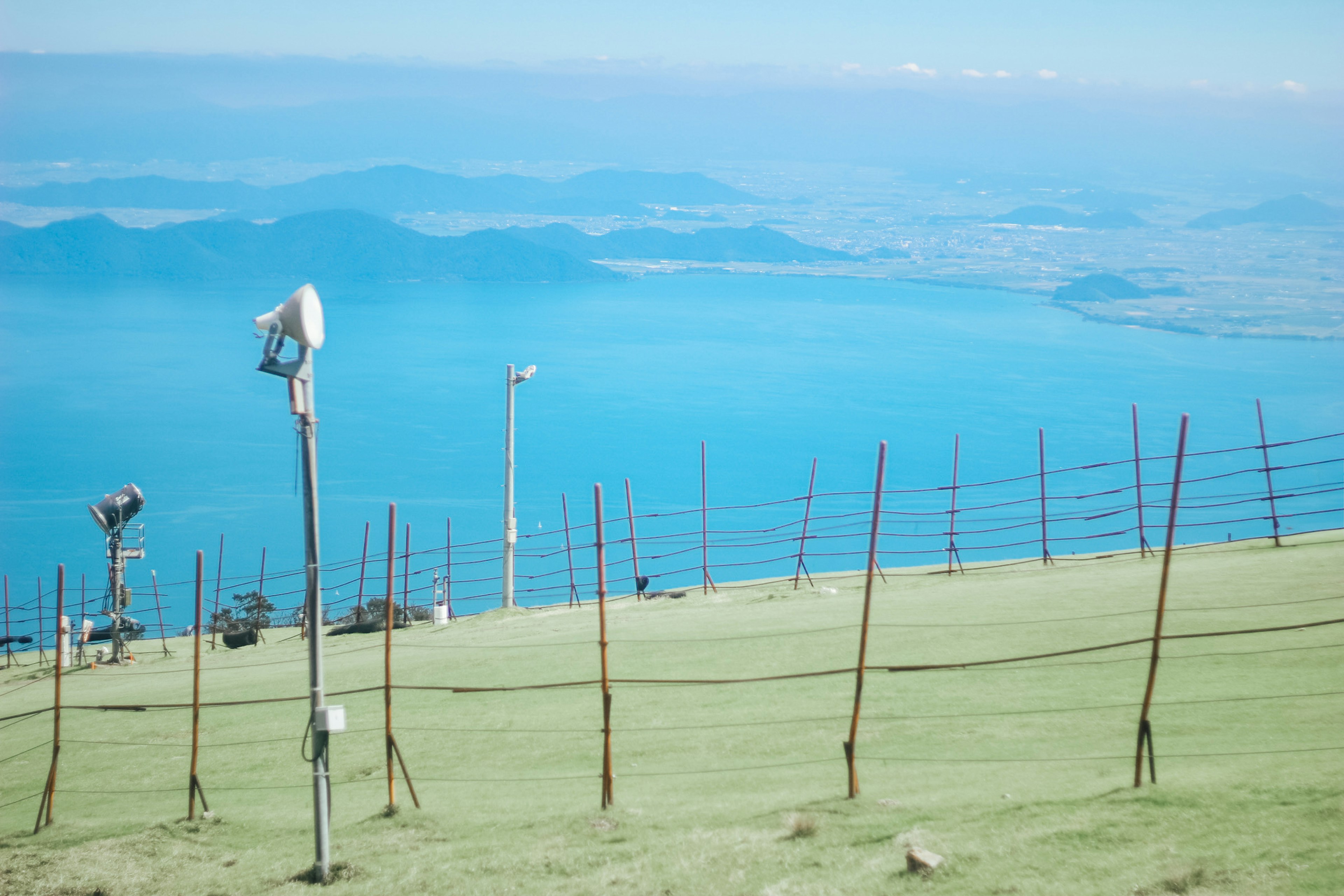 Vista panorámica de una colina con vista al mar azul y cielo con altavoces y postes visibles