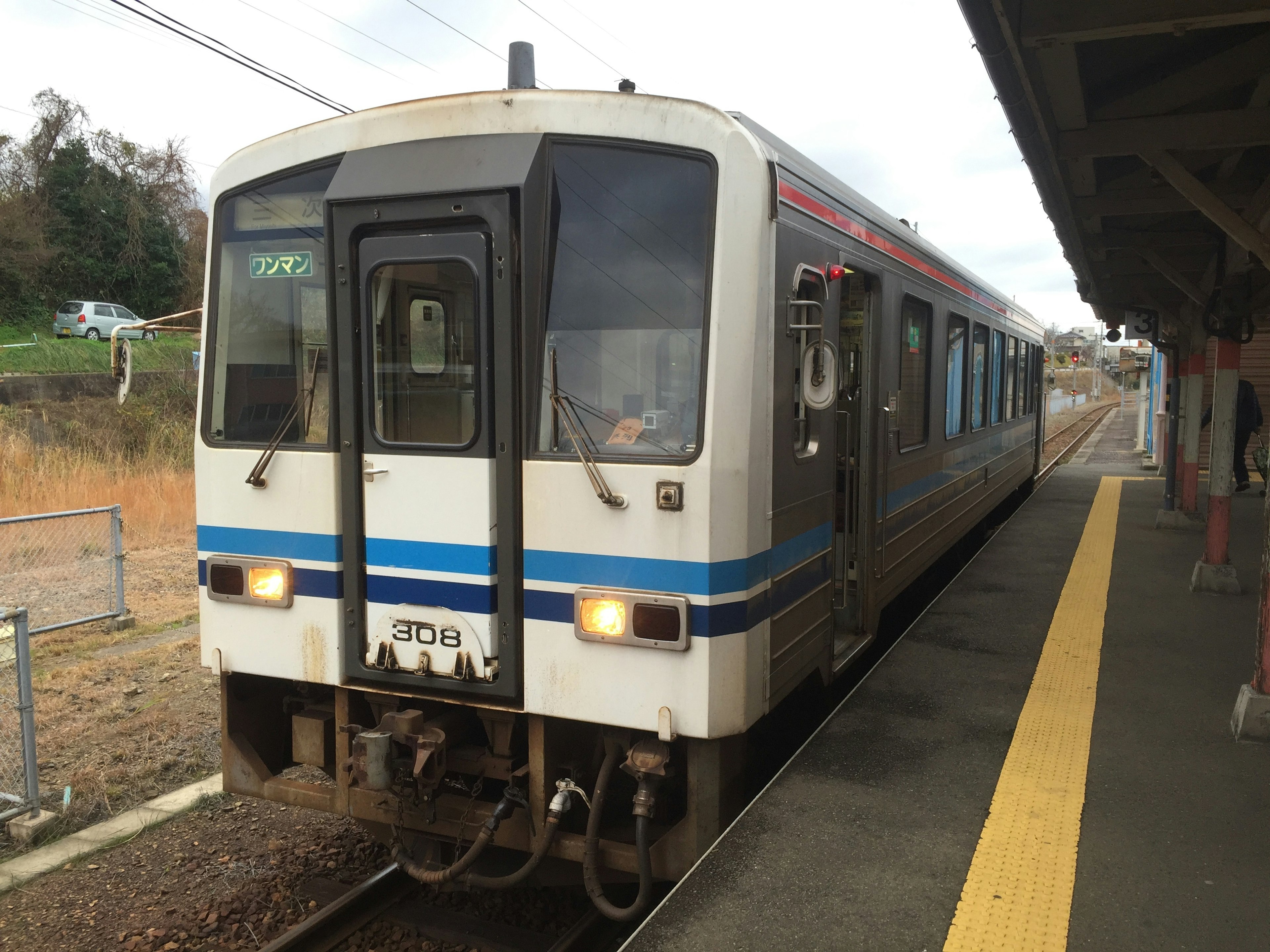 白い電車が駅に停車中で周囲に草原と線路が見える