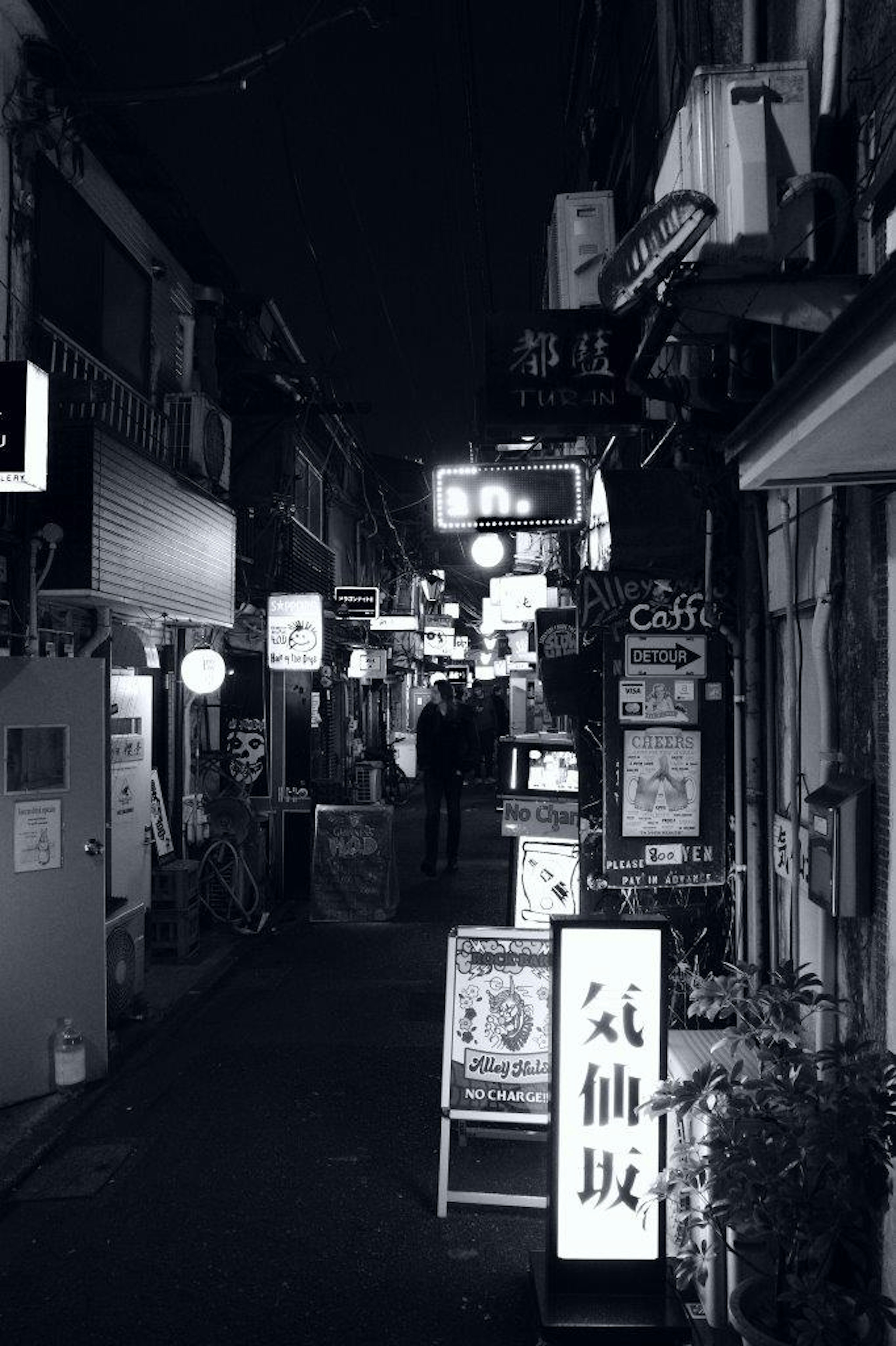 Narrow street at night with illuminated signs and storefronts