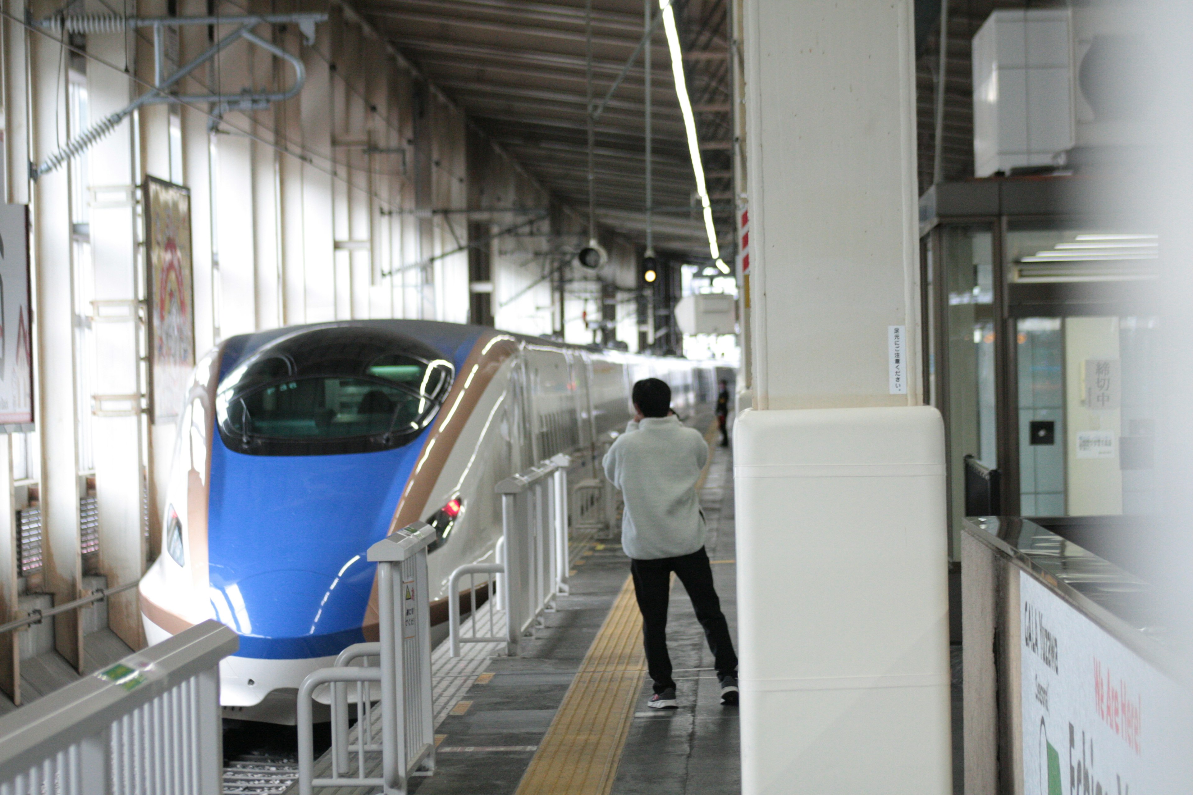 Blue Shinkansen train stopped at a station with a person in white clothing