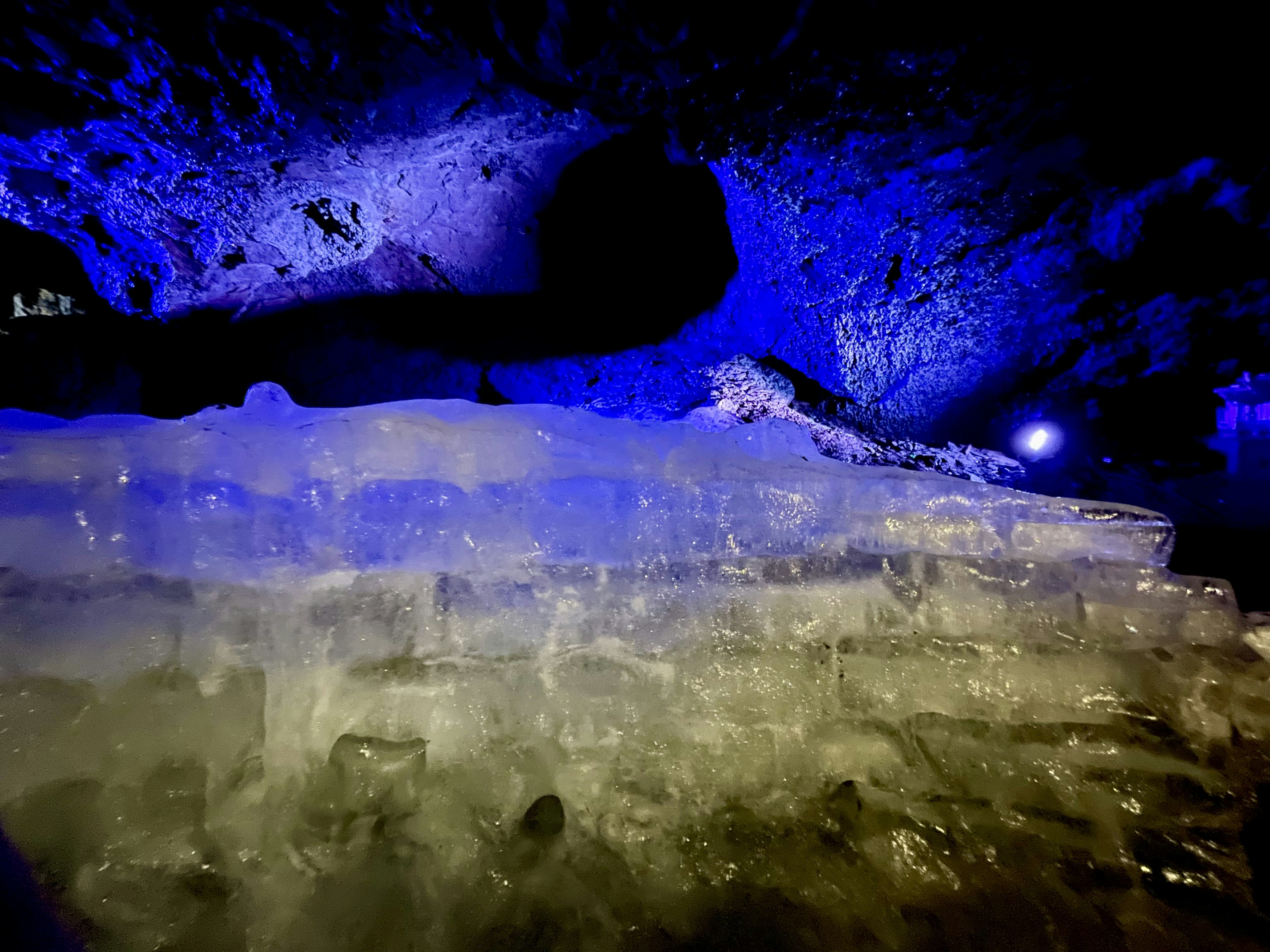 青い光に照らされた氷の層がある洞窟の内部