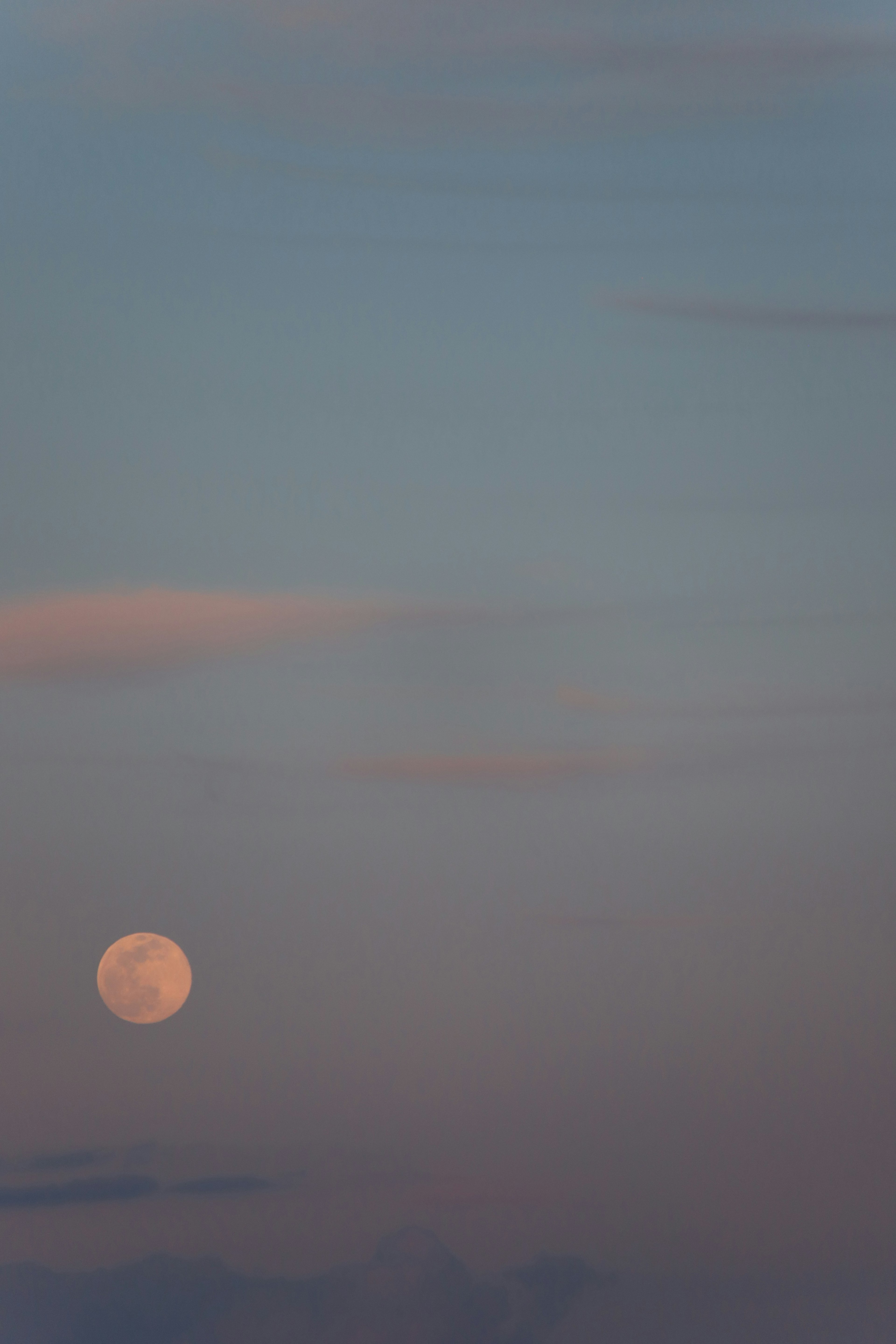 Large full moon against a soft pastel sky with subtle clouds