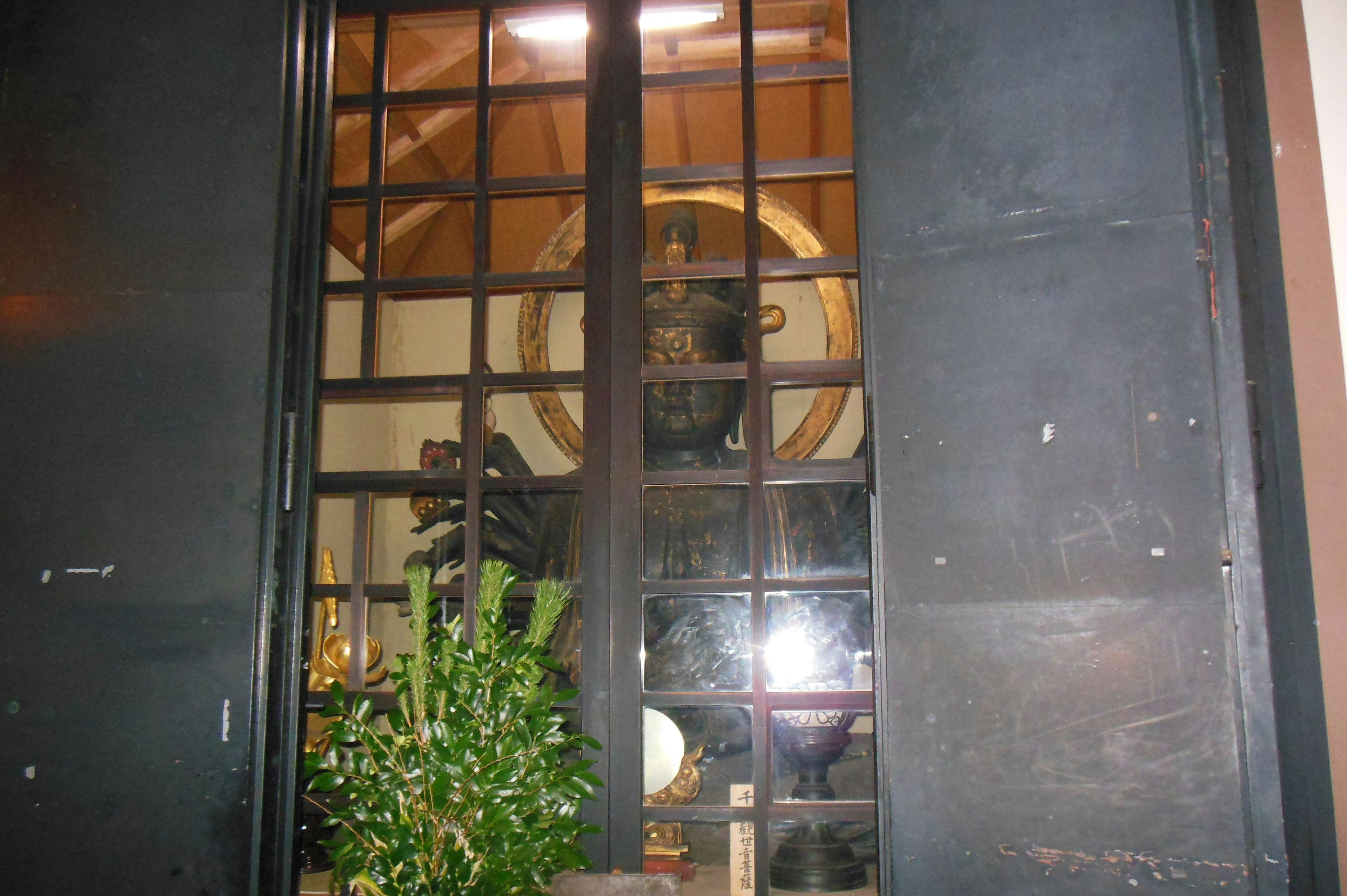 Buddha statue visible through black window frame with plants