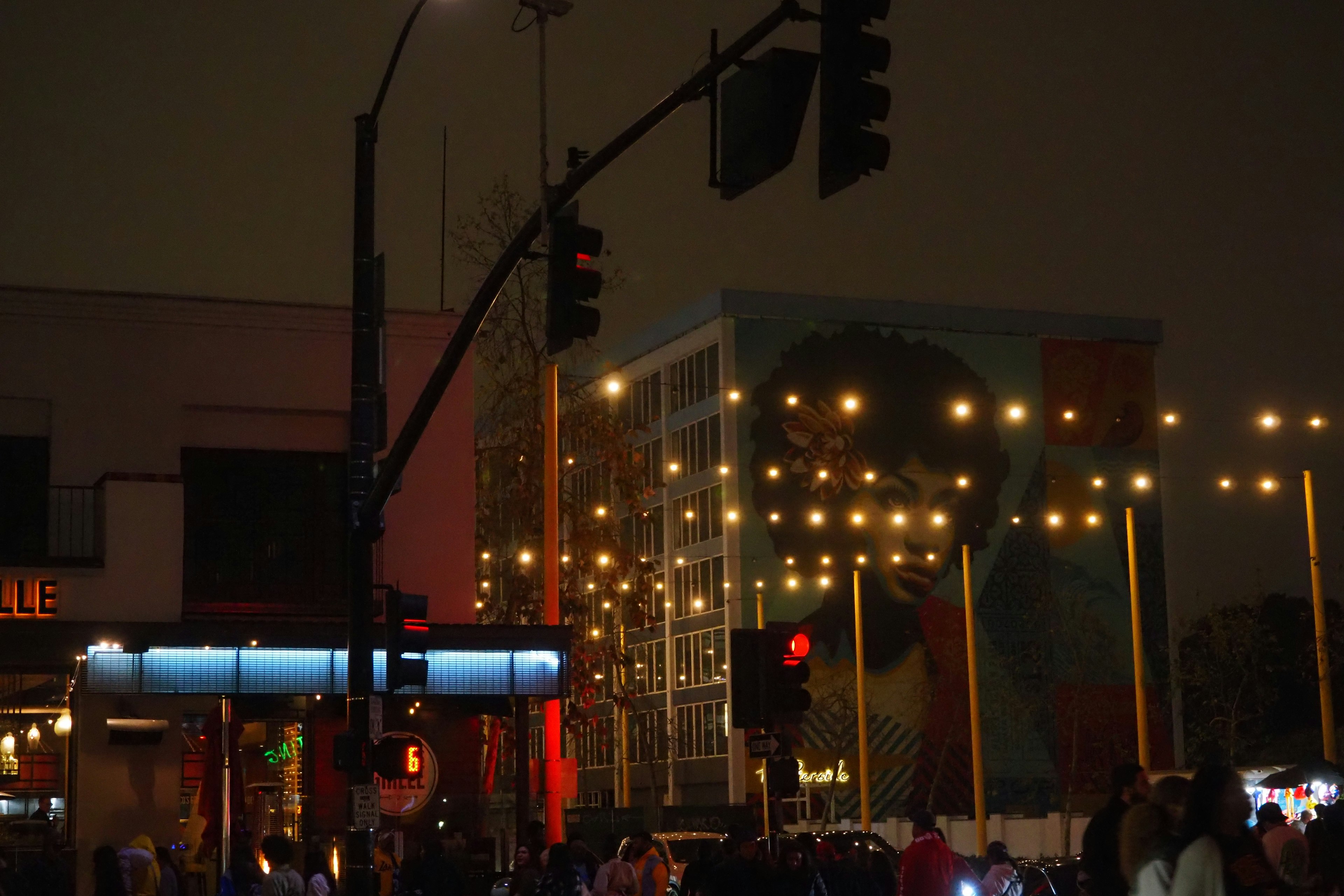 Semáforo de noche con personas reunidas luces coloridas y arte urbano al fondo