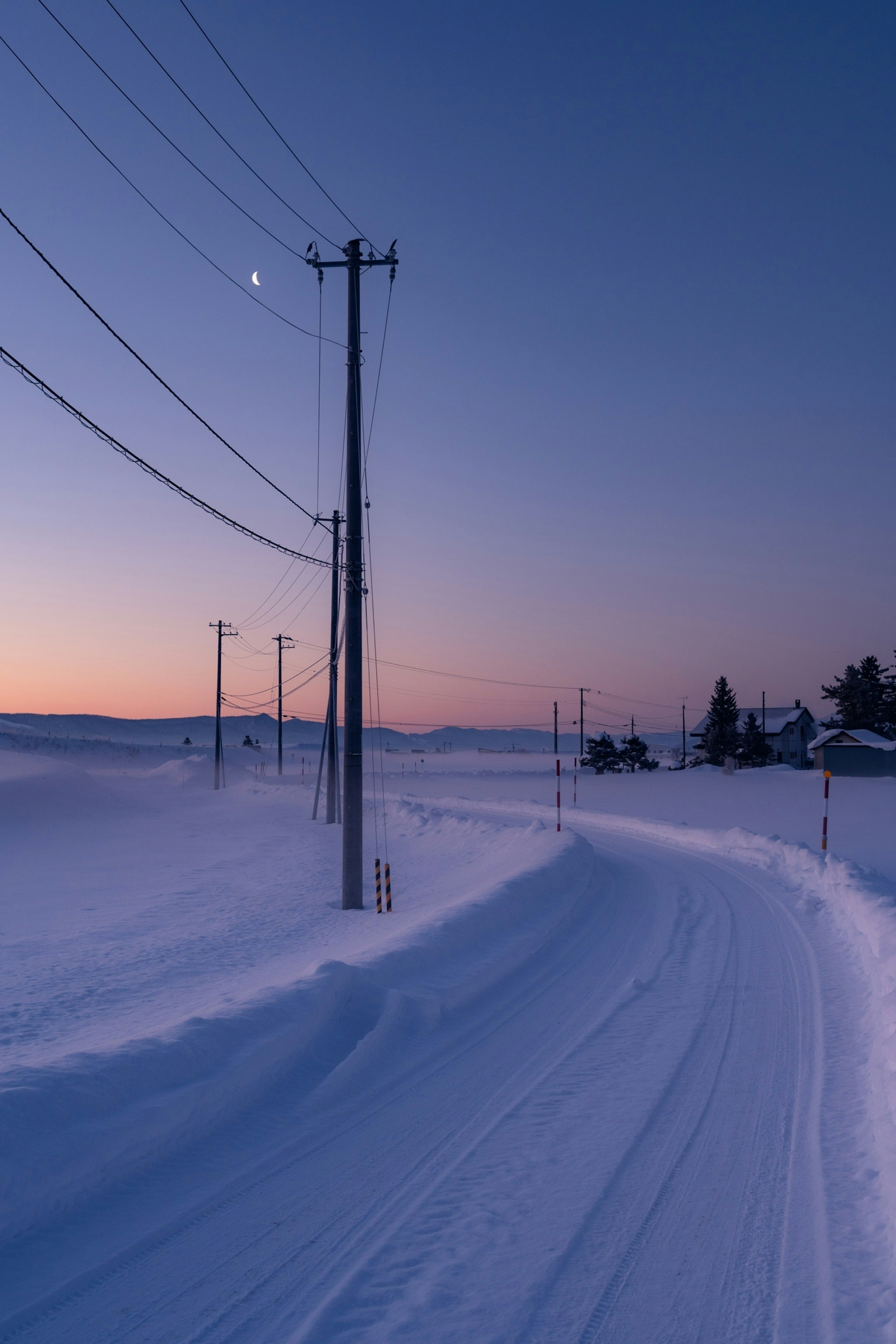 Route enneigée avec des poteaux électriques sous un ciel crépusculaire