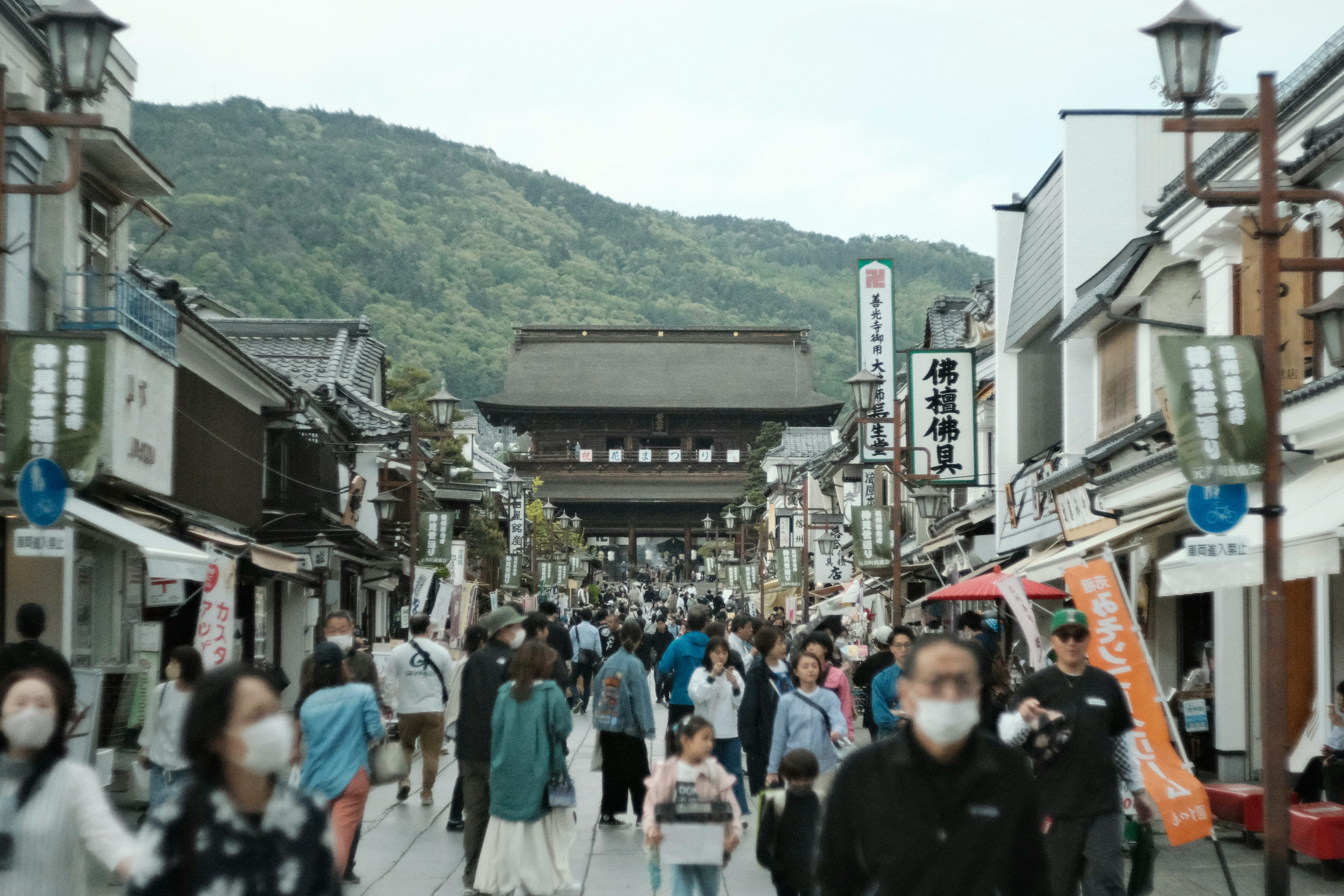 賑やかな通りに人々が集まり、山が背景に広がる風景