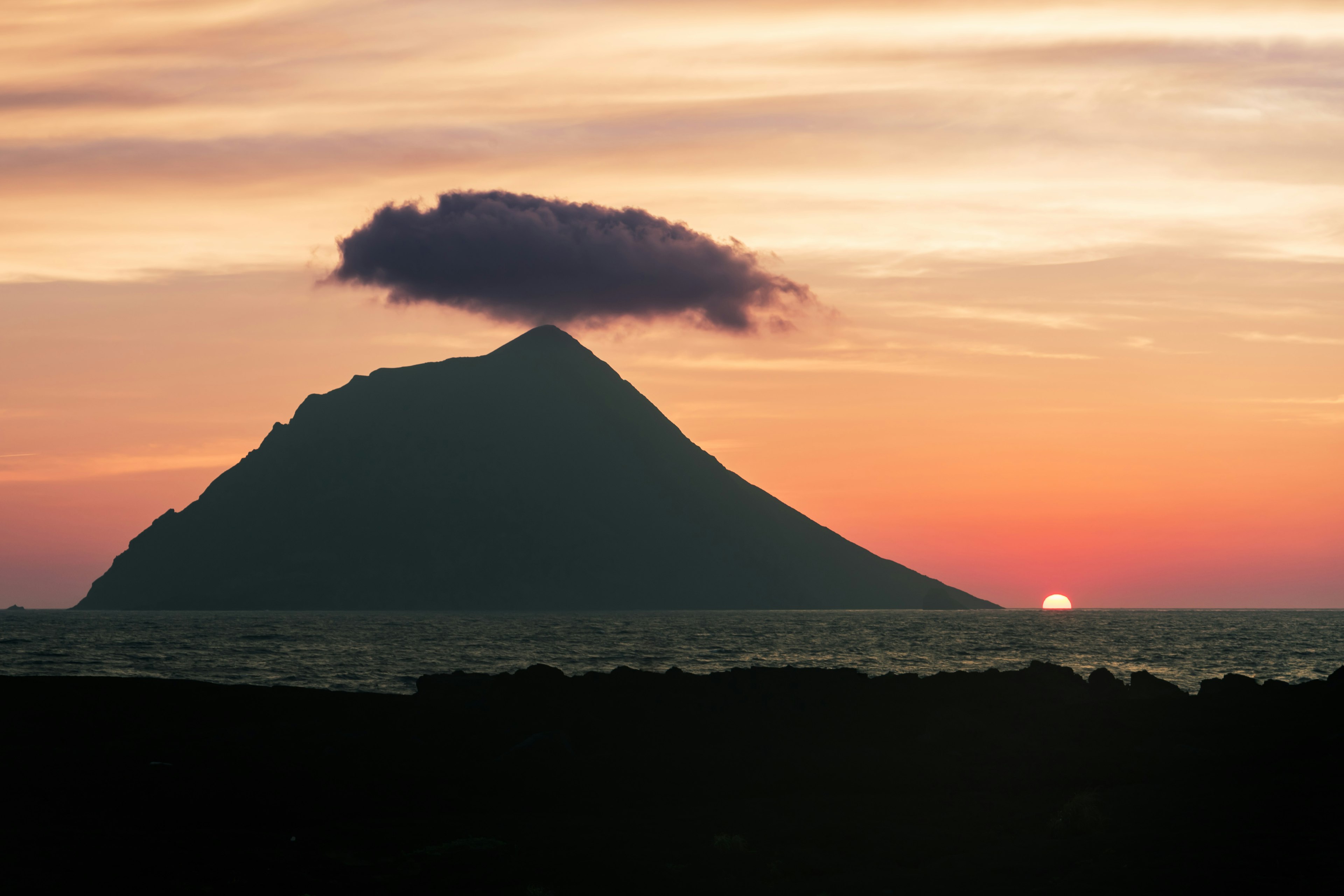 Silhouette eines Berges mit einer Wolke und Sonnenuntergang im Hintergrund