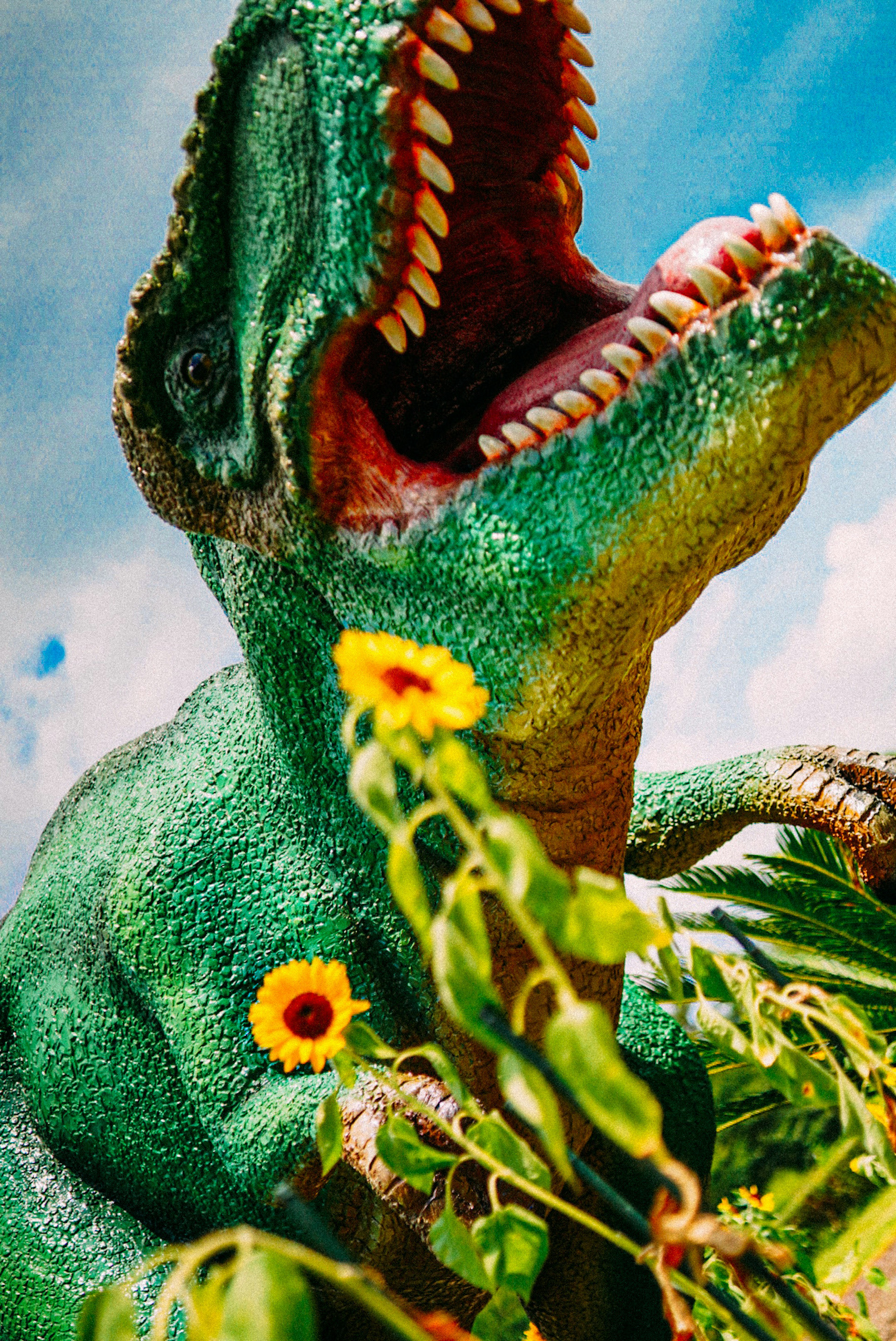 Un dinosauro verde che si erge tra i fiori con la bocca aperta