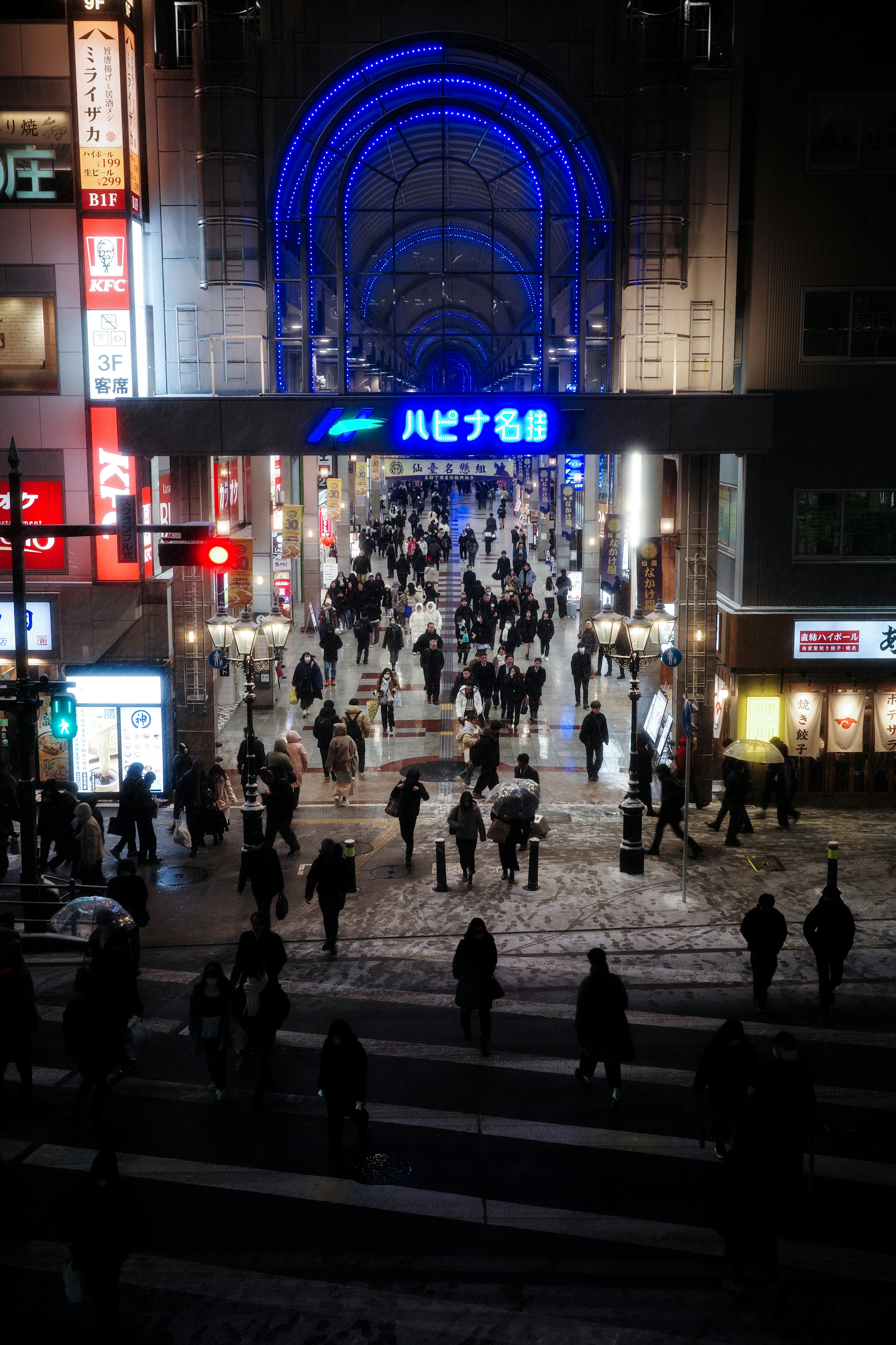 Vue nocturne d'une rue animée avec des gens marchant sous une arche bleue