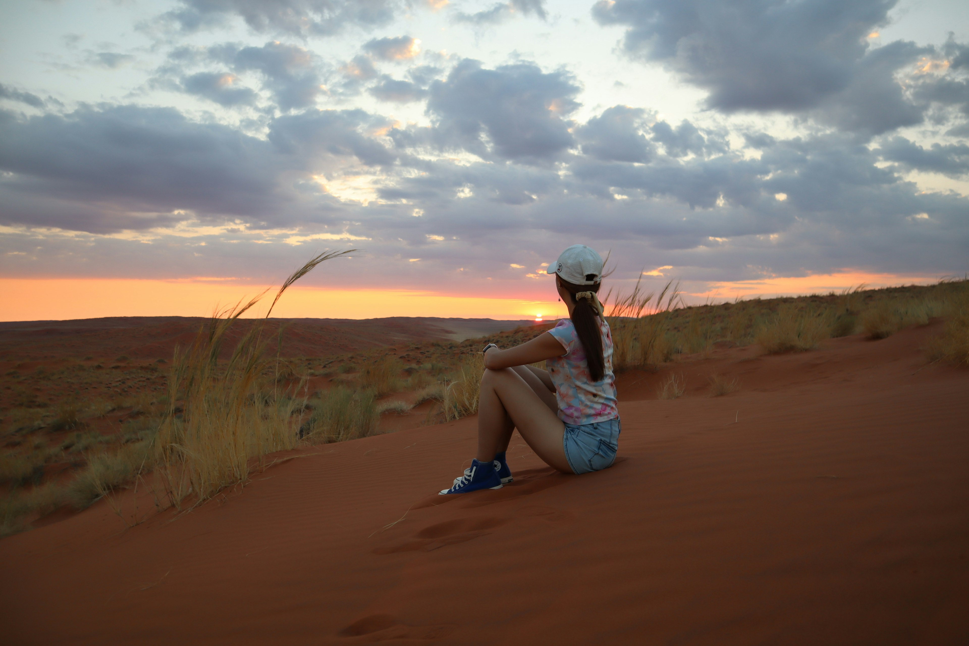 Una donna seduta su una duna di sabbia al tramonto