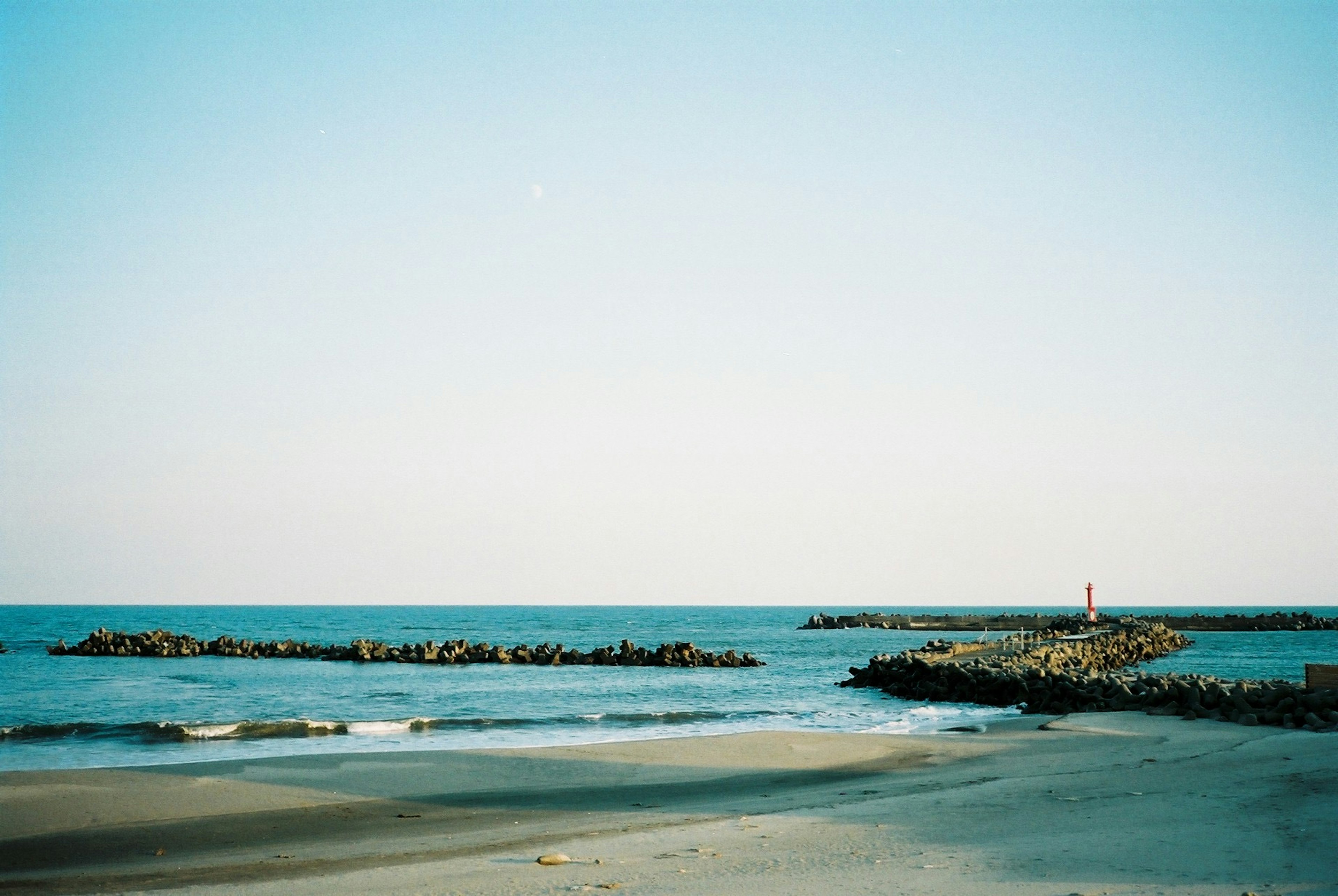 Scène de mer calme et ciel bleu avec jetée rocheuse et phare rouge