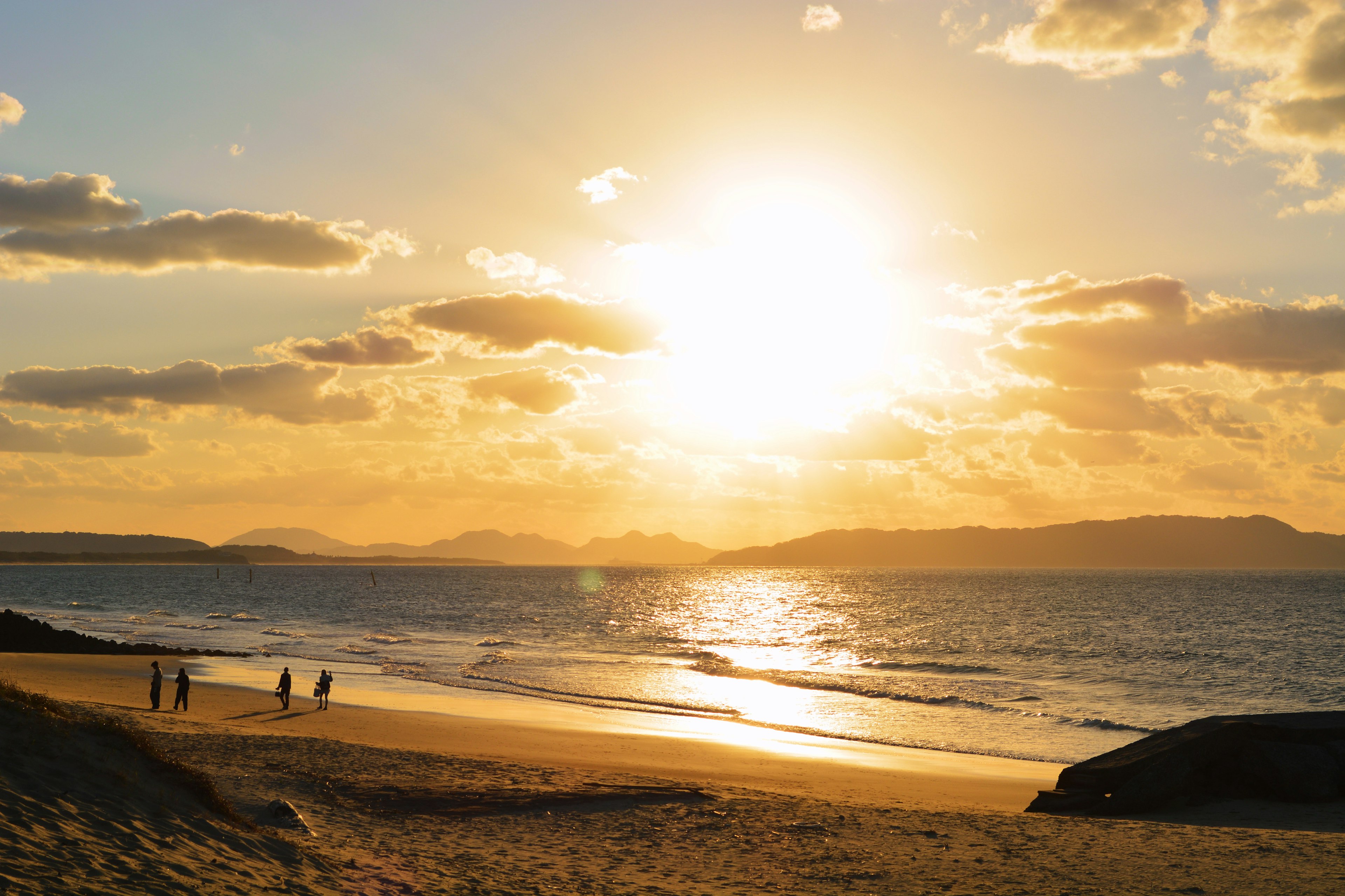 Paisaje de playa con atardecer sobre el océano personas caminando sobre la arena