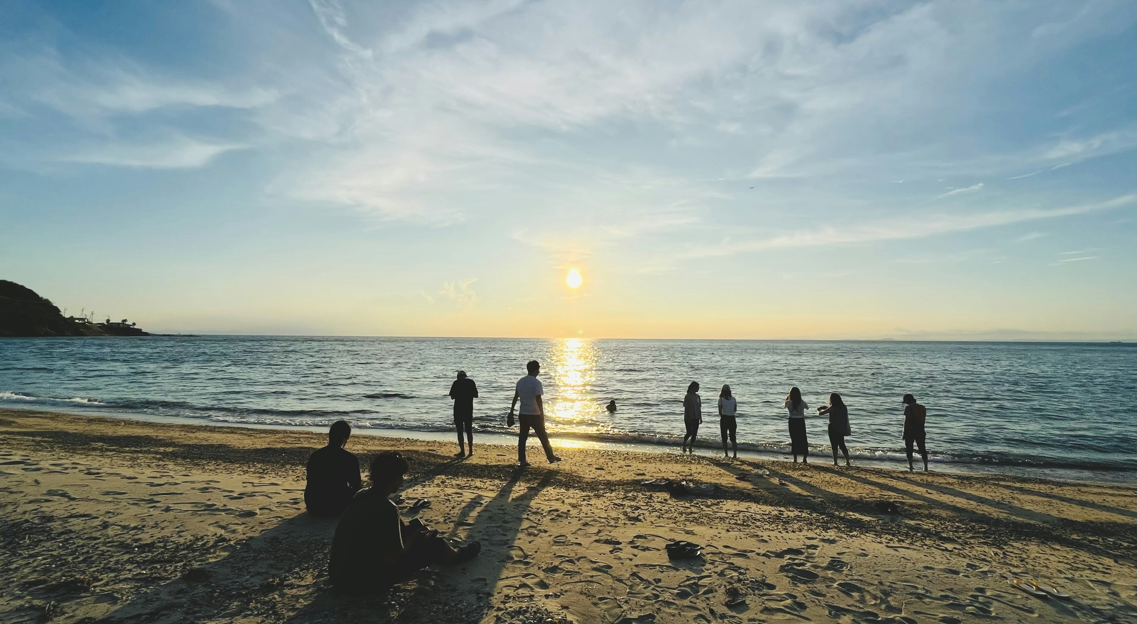 夕日を背景に海で遊ぶ人々とビーチに座る人