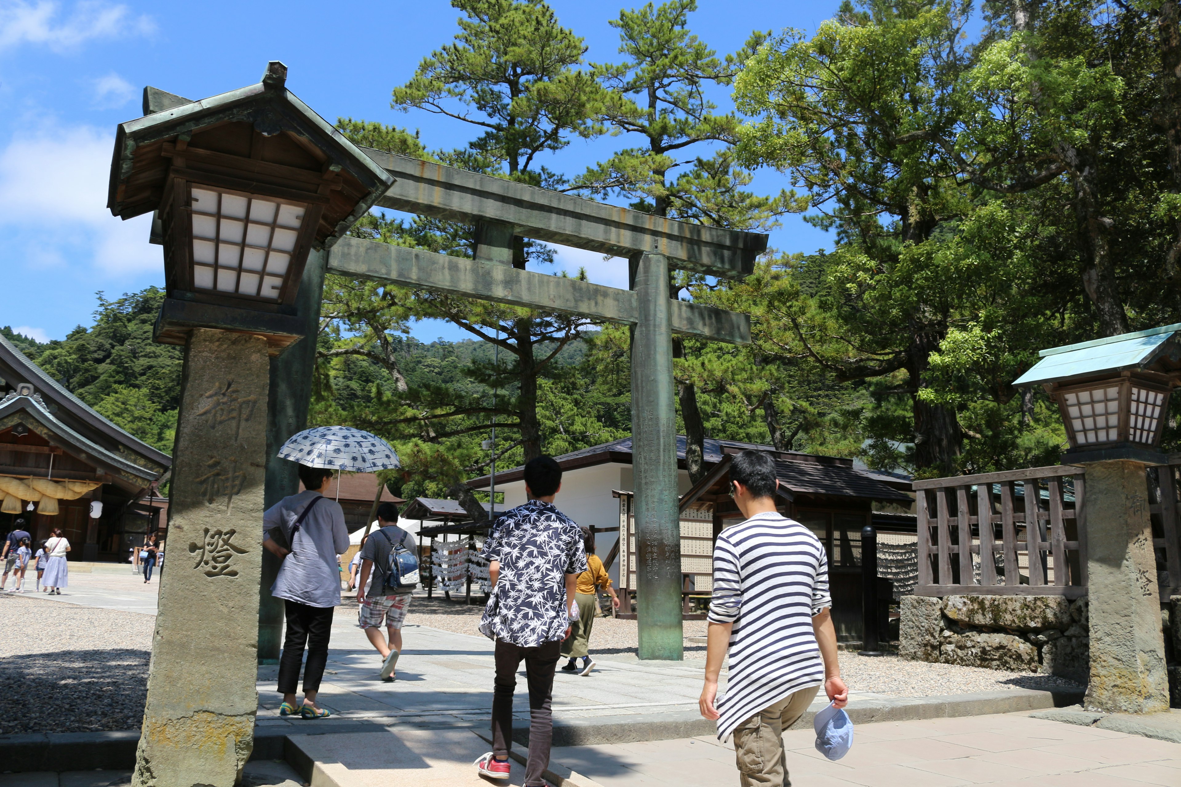 Des personnes marchant à travers un torii entouré de verdure et d'un ciel bleu clair