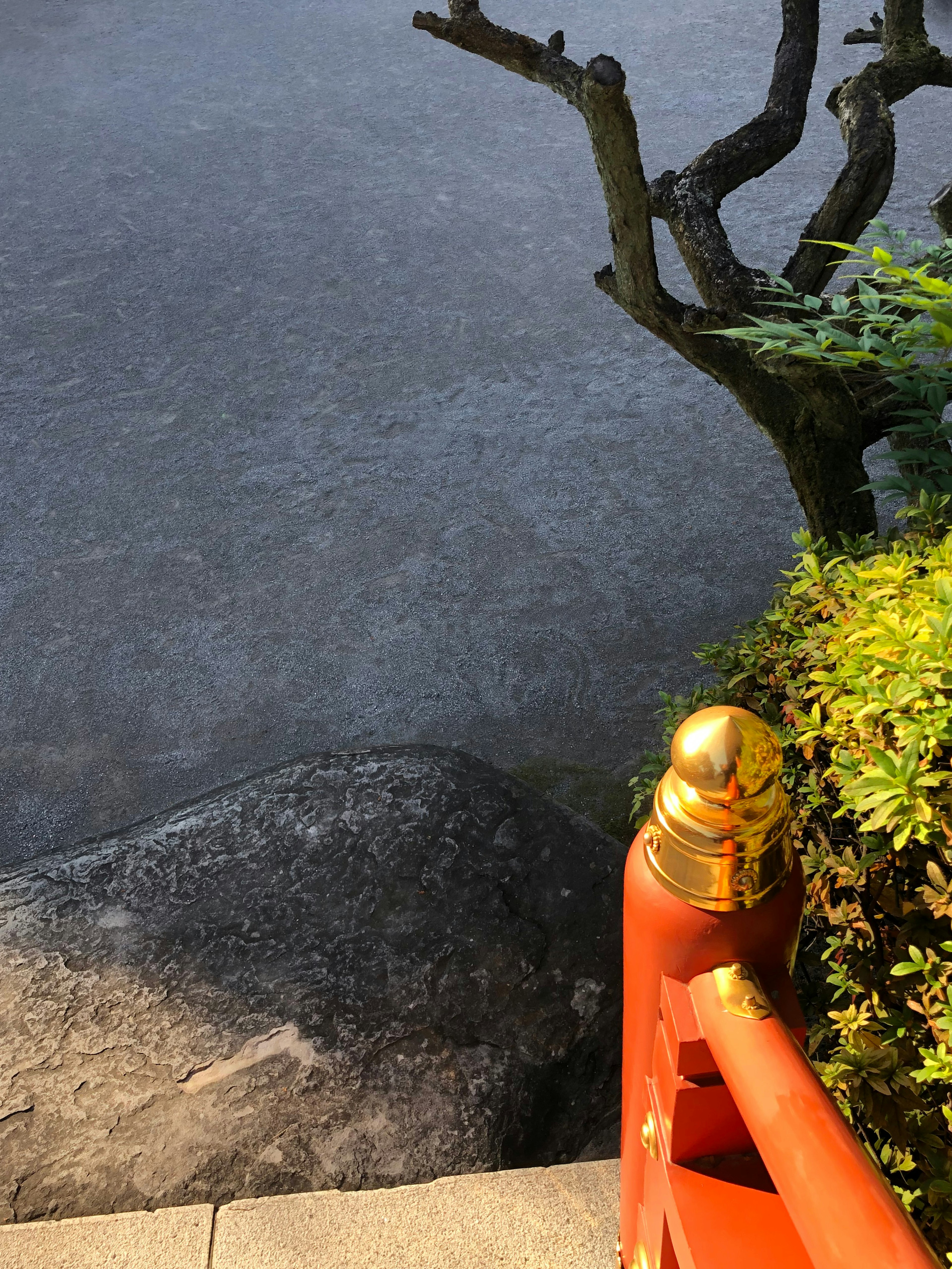 A section of a landscape featuring a red railing with a golden ornament and green foliage