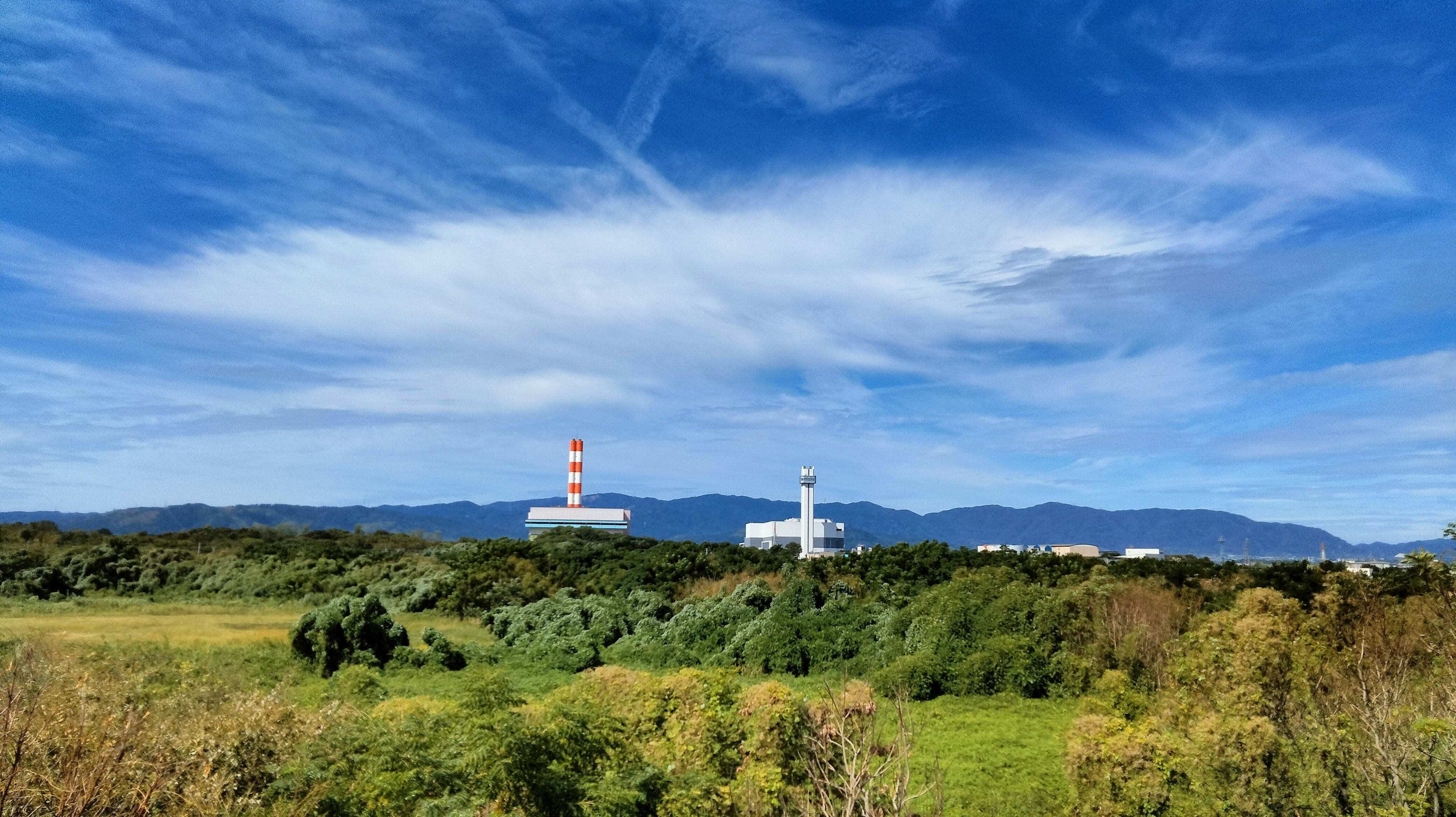 Structures d'usine sous un ciel bleu avec des nuages blancs et un paysage vert