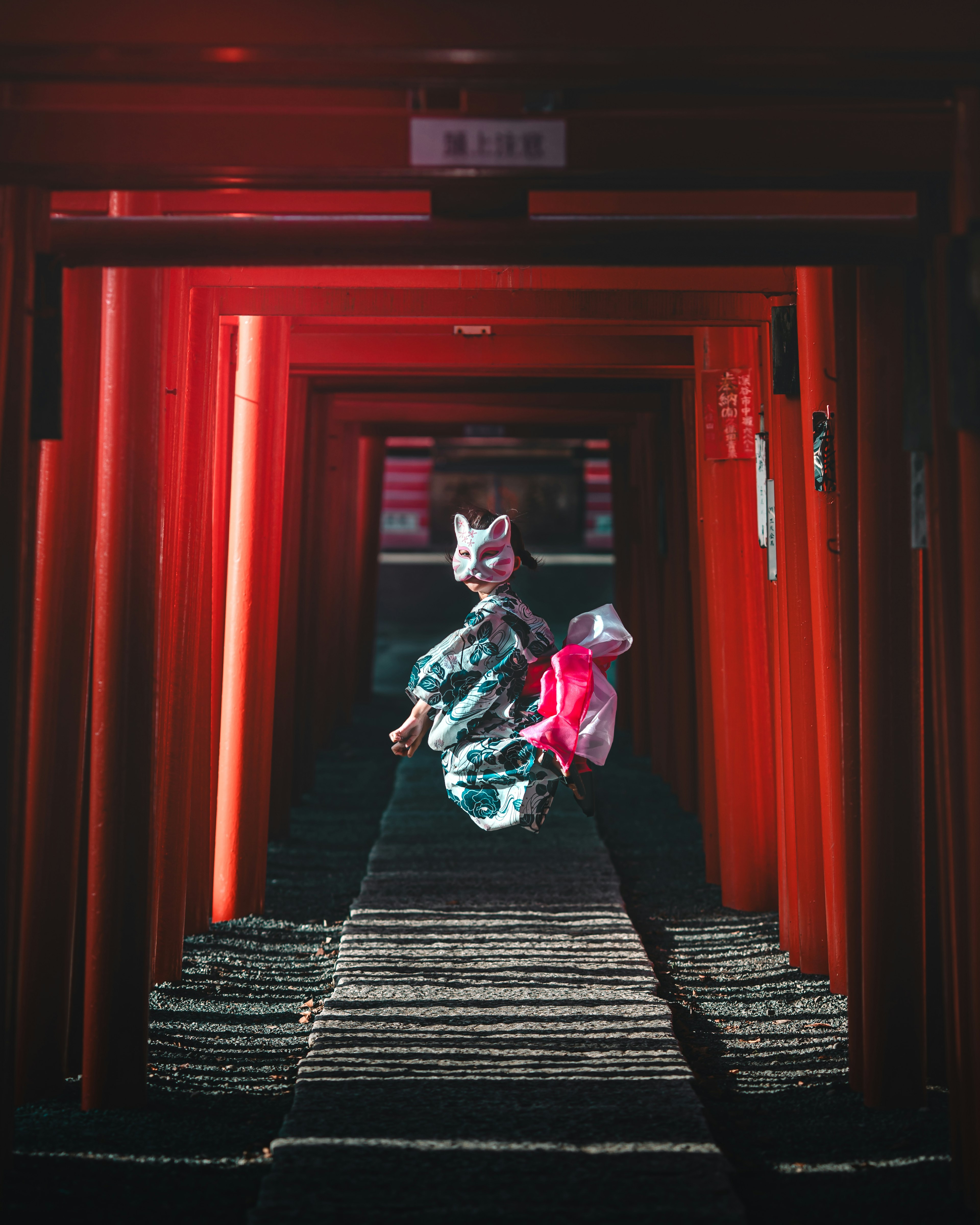 Donna in kimono con maschera di volpe che corre attraverso un tunnel di torii rossi