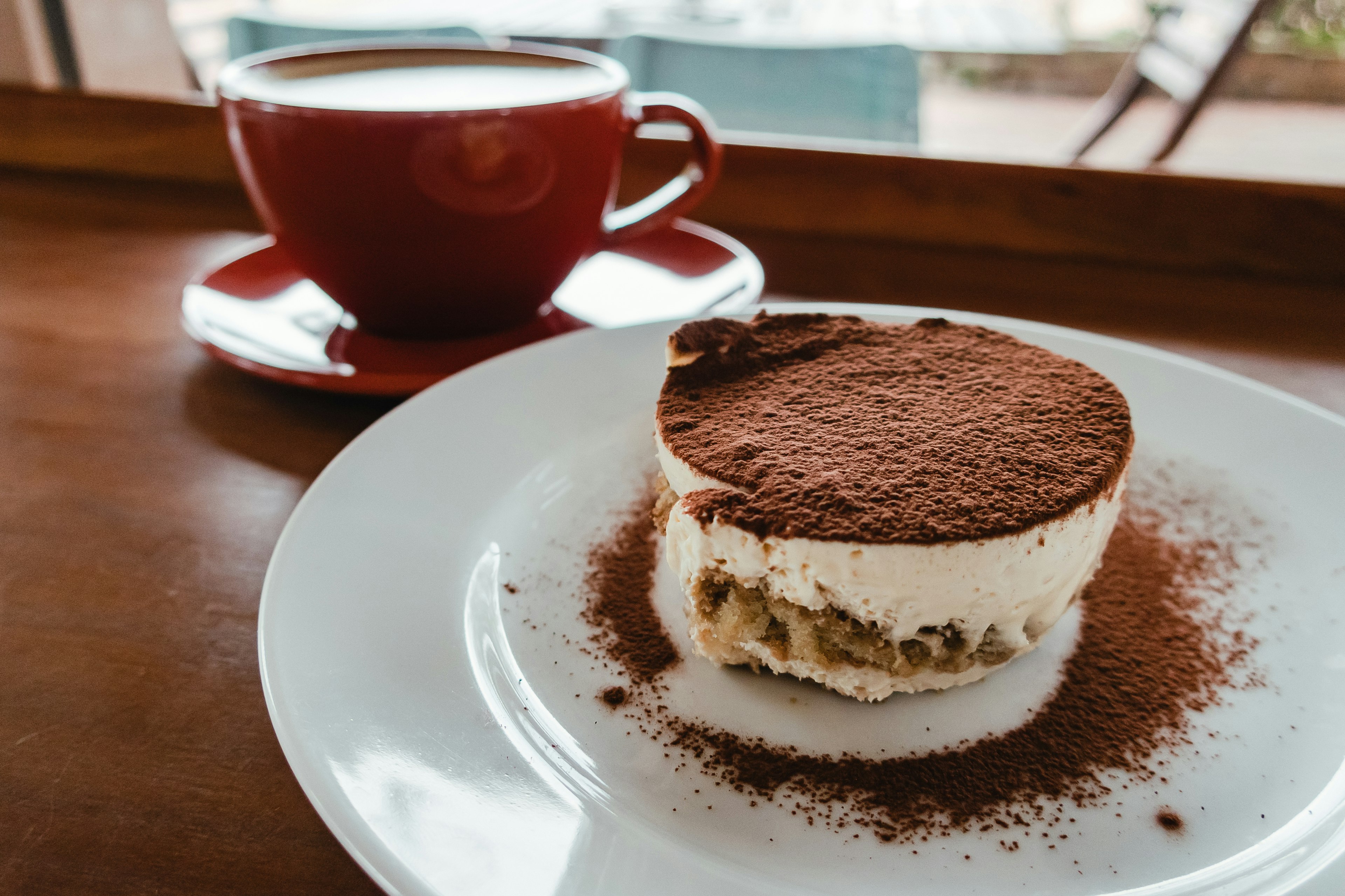 Coffee cup next to a slice of tiramisu on a white plate