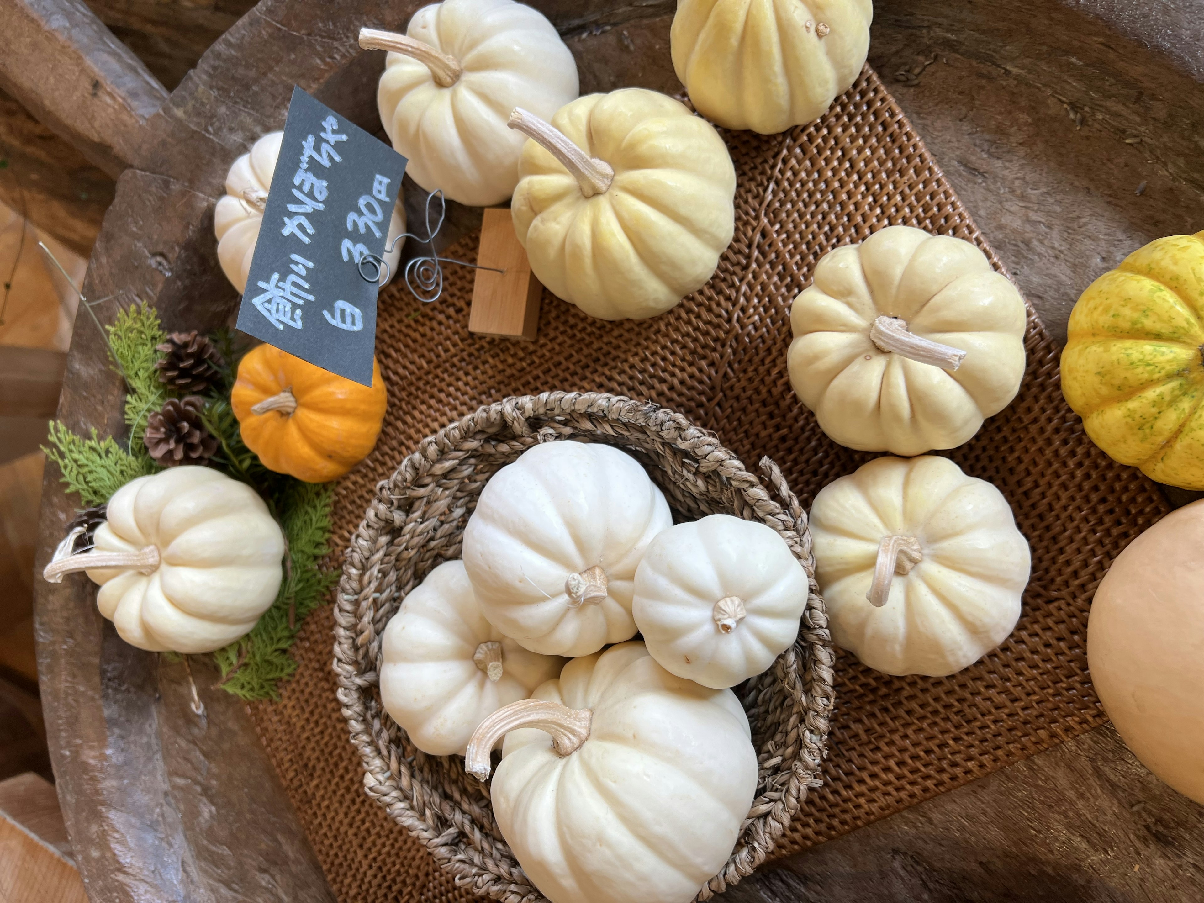 Scena di zucche bianche disposte su un tavolo cesto con zucche e una piccola zucca arancione alcune foglie verdi e un appunto su una lavagna nera