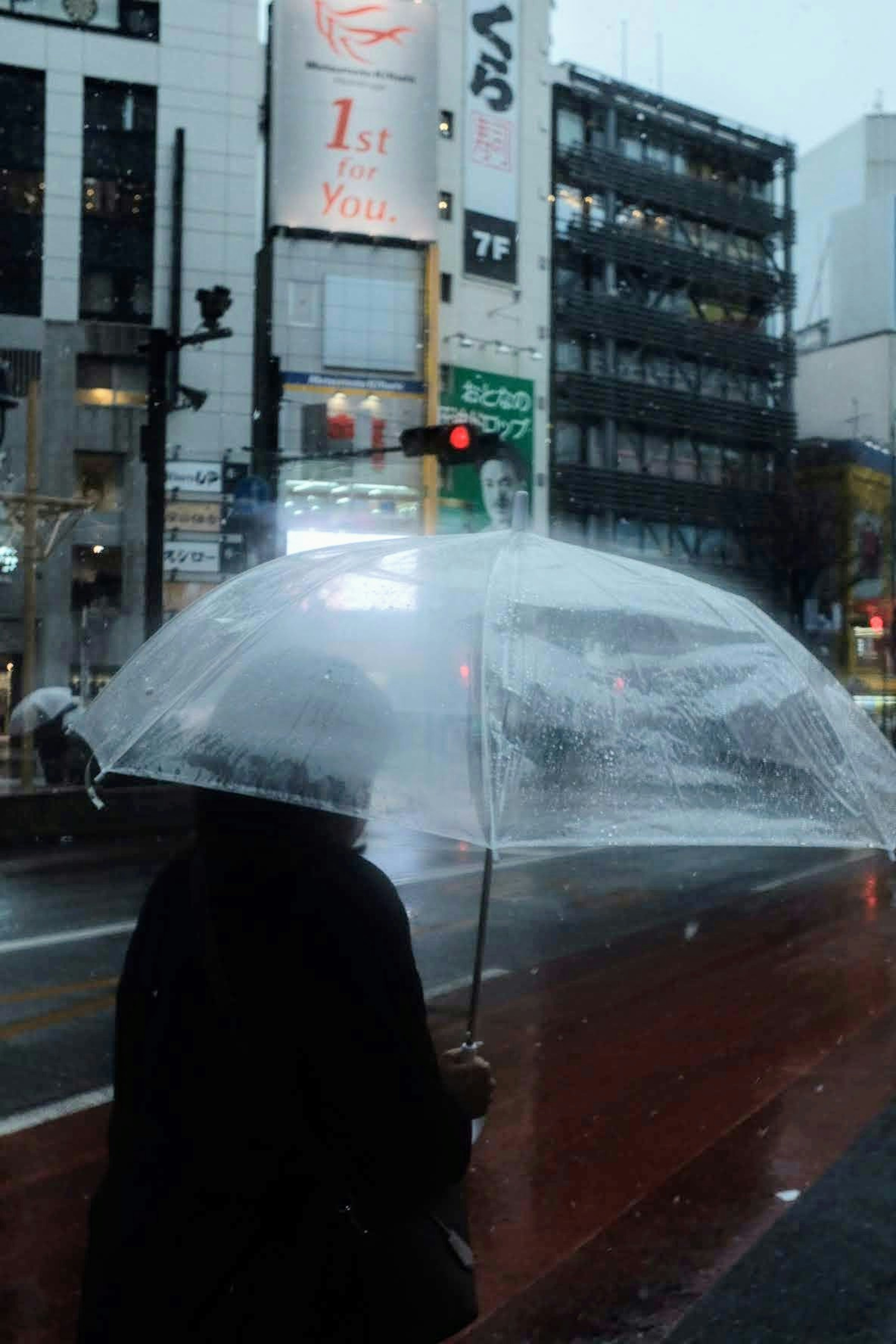 Silhouette of a person holding a transparent umbrella in the rain city signs and buildings in the background