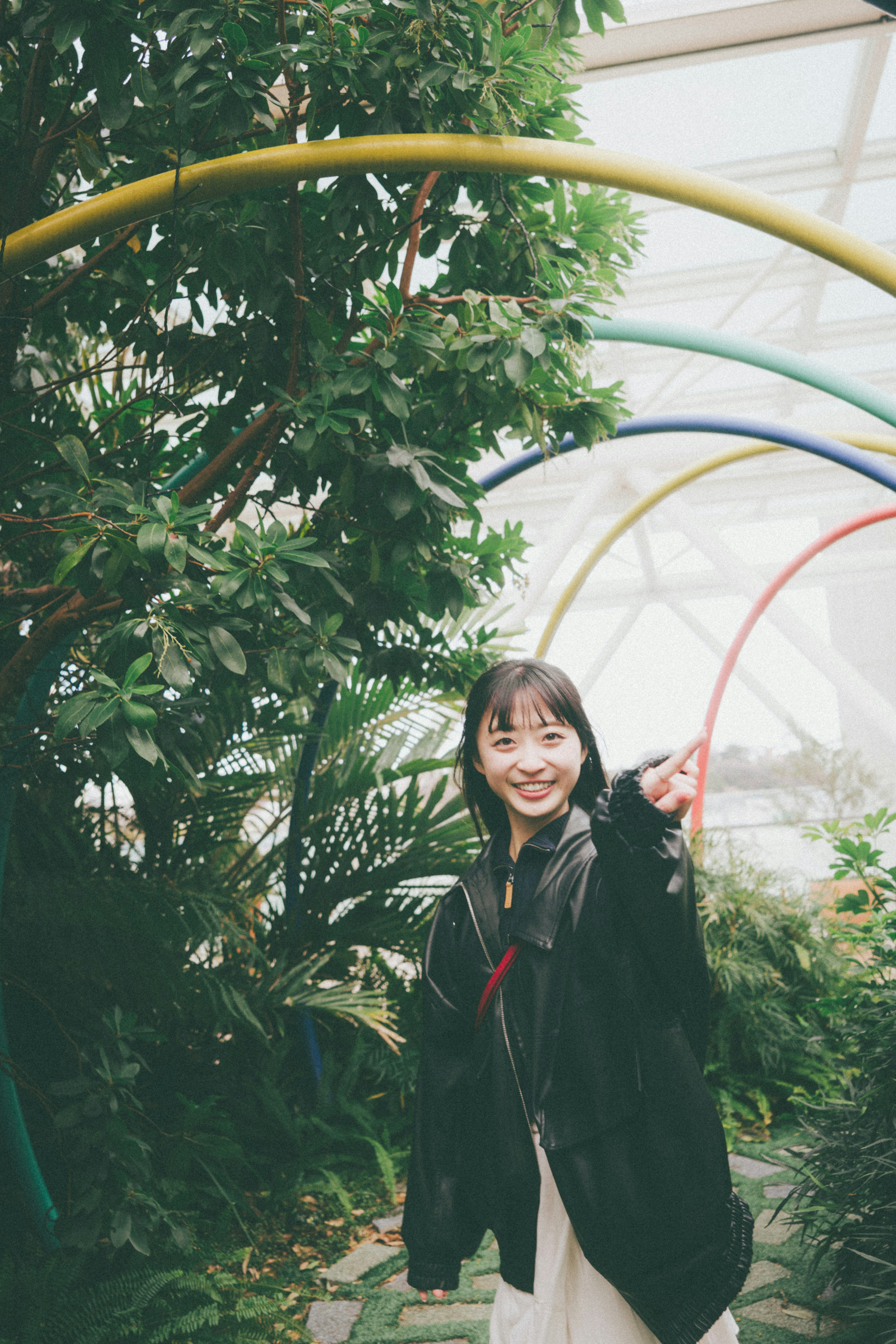 Mujer sonriente señalando en un arco colorido rodeado de plantas verdes