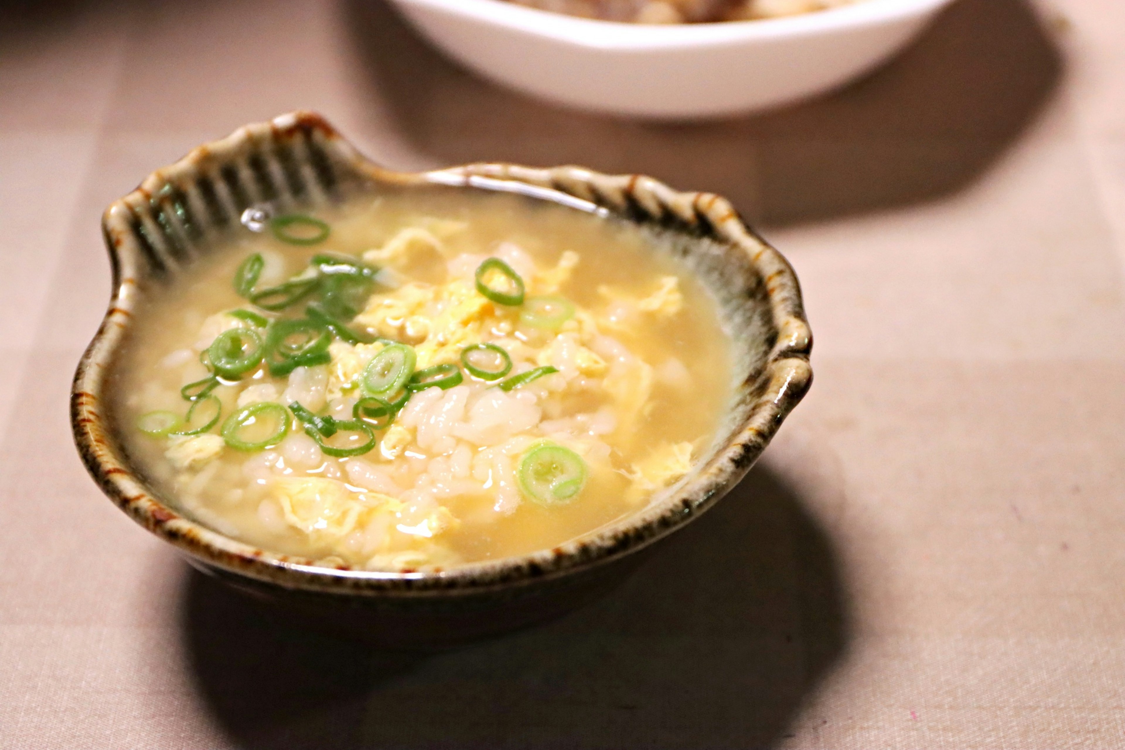 Warm porridge soup topped with green onions served in a beautiful bowl