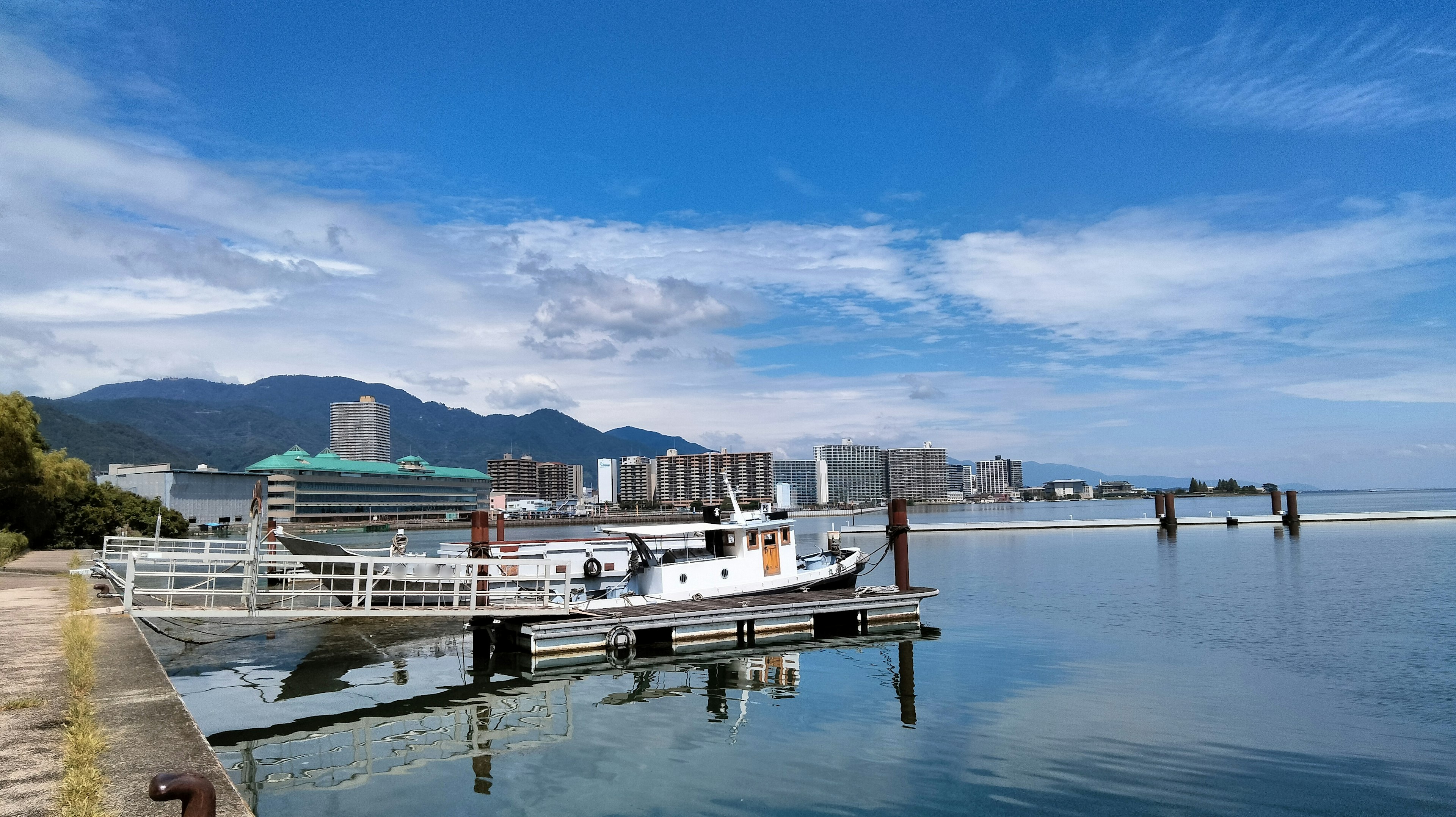 Un barco atracado junto al mar tranquilo bajo un cielo azul claro y edificios distantes