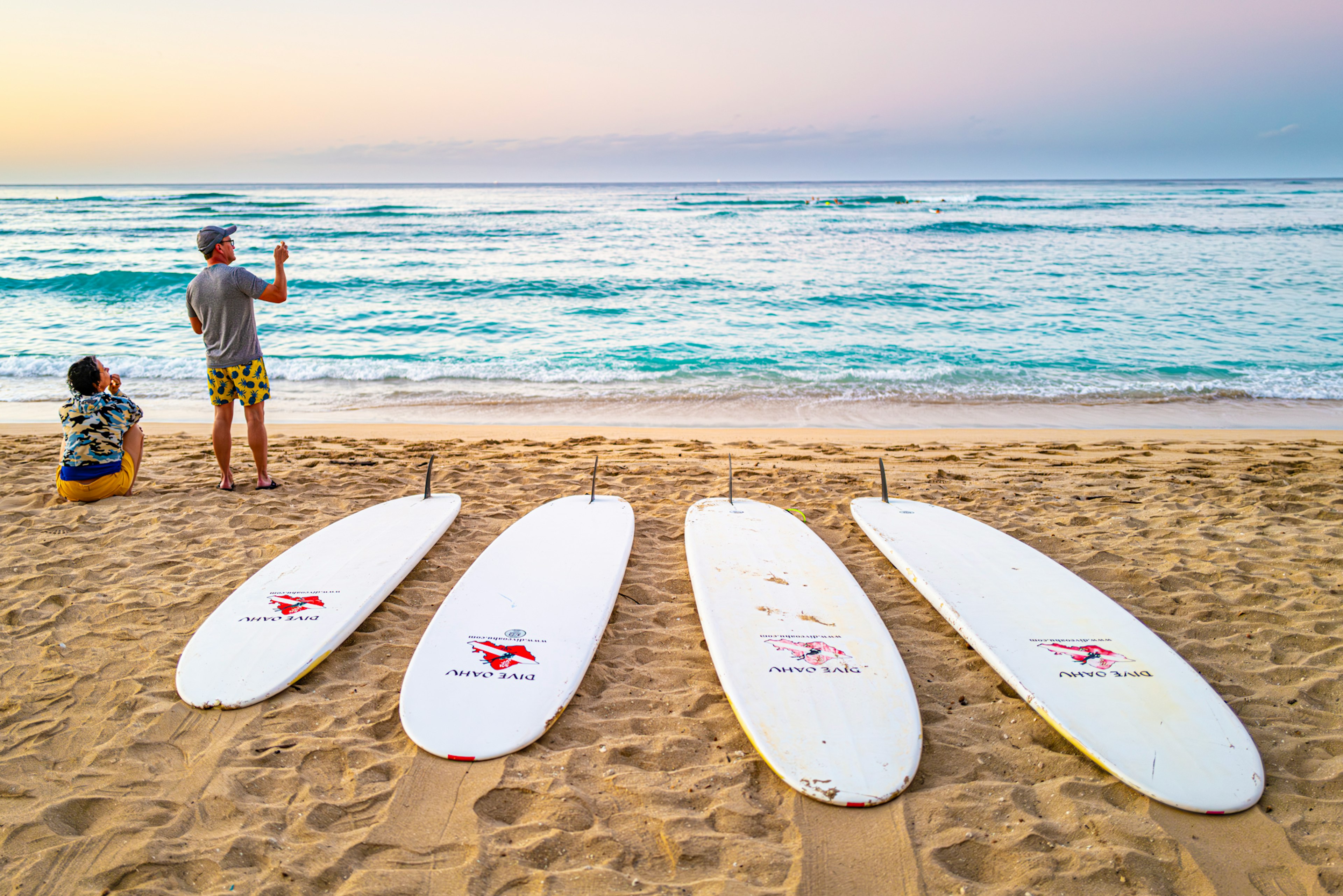 Surfistas preparándose en la playa con tablas de surf alineadas y olas del océano de fondo