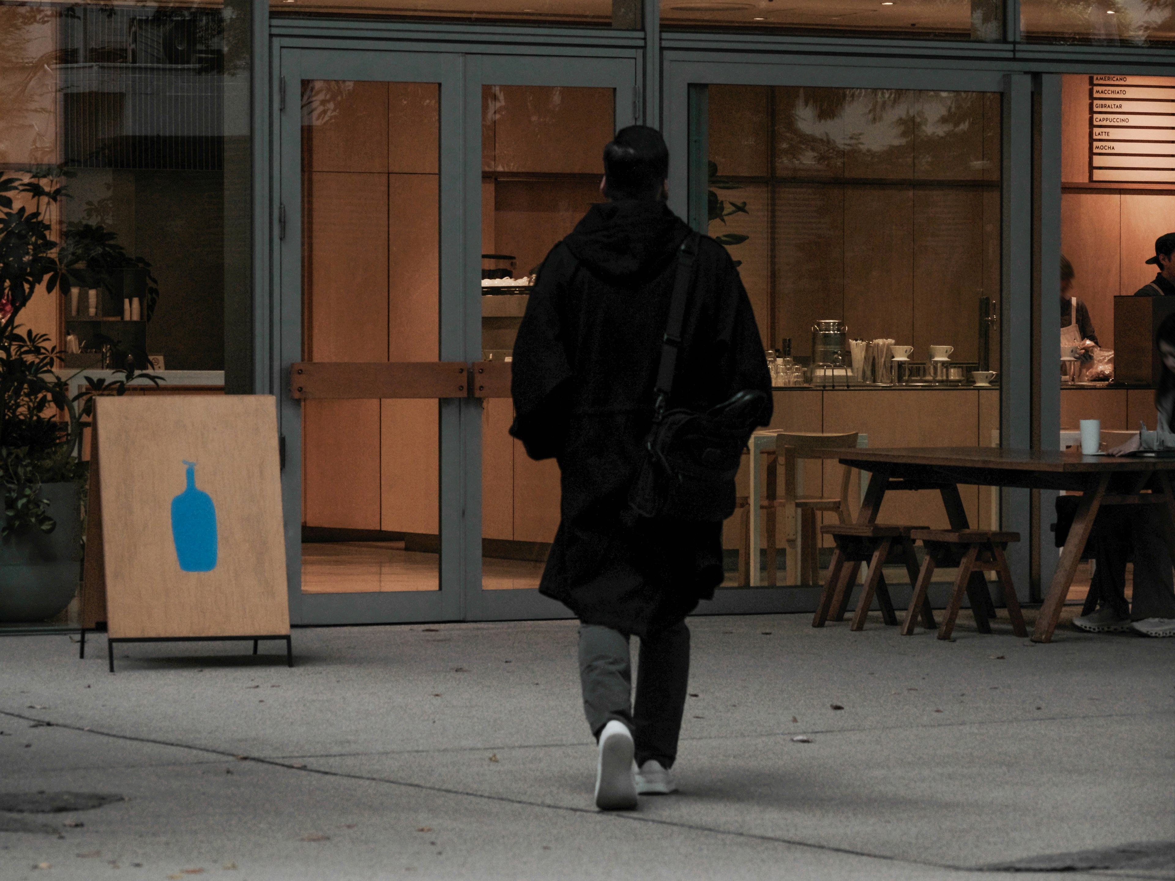 Eine Person in einem schwarzen Mantel geht auf den Eingang eines Cafés zu