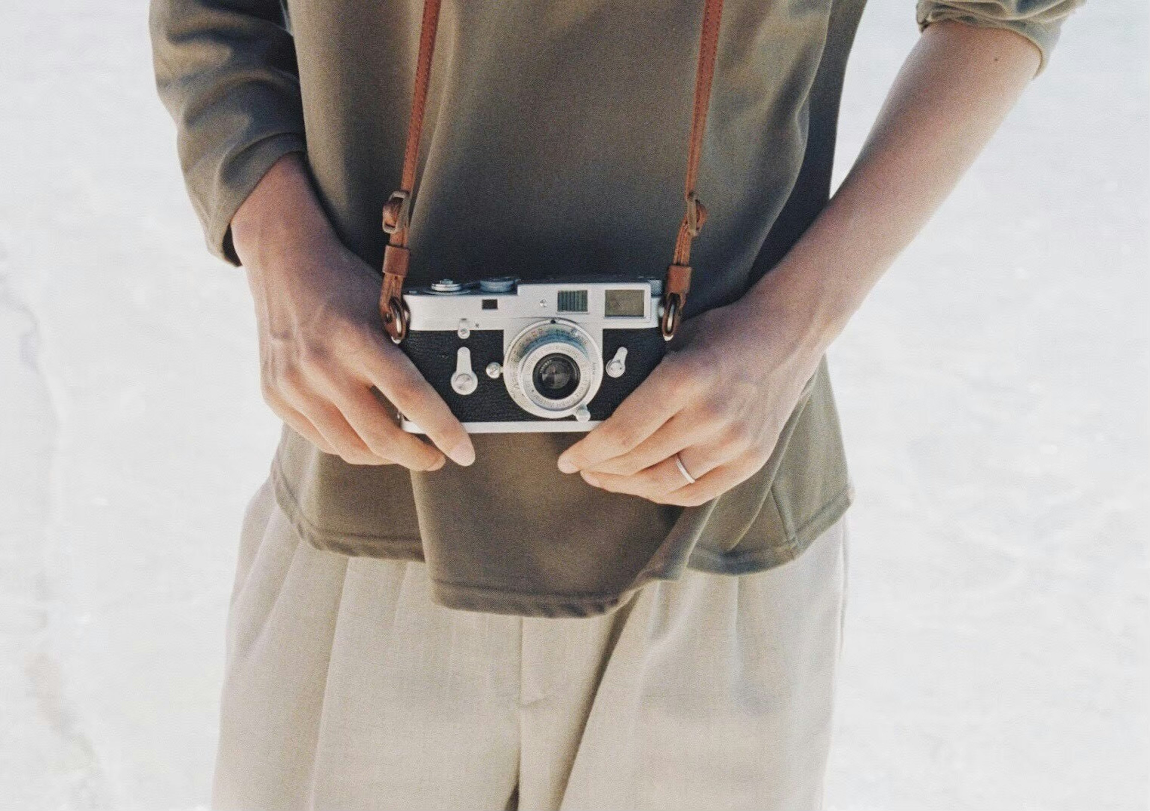 Primo piano di una persona che tiene una macchina fotografica con una tracolla