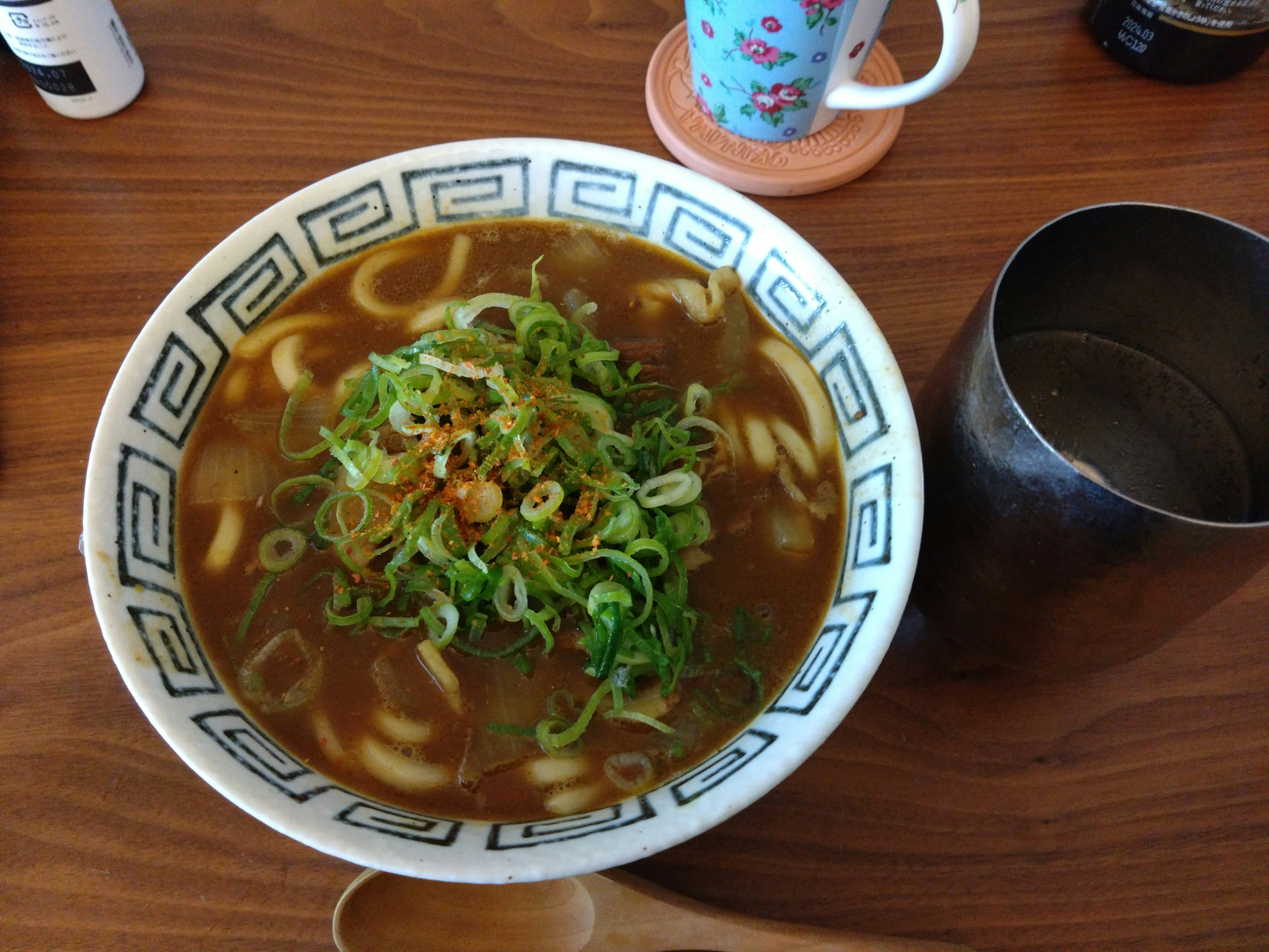 緑のねぎがたっぷりのうどんのボウルと飲み物があるテーブル