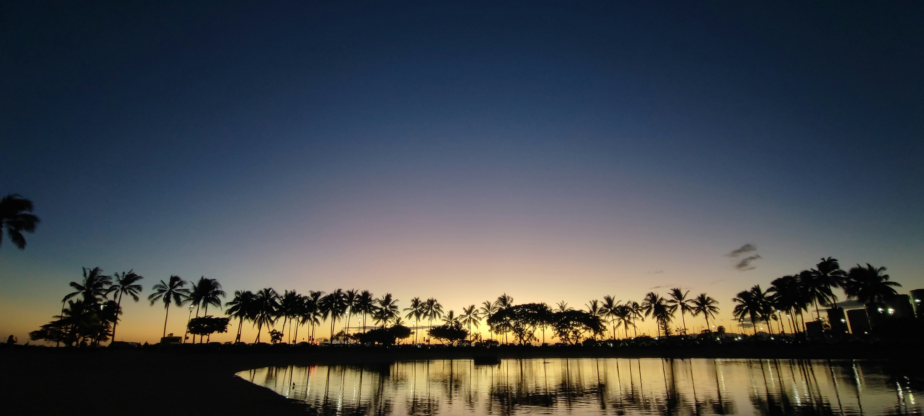 Acqua serena che riflette un cielo al tramonto con palme in silhouette