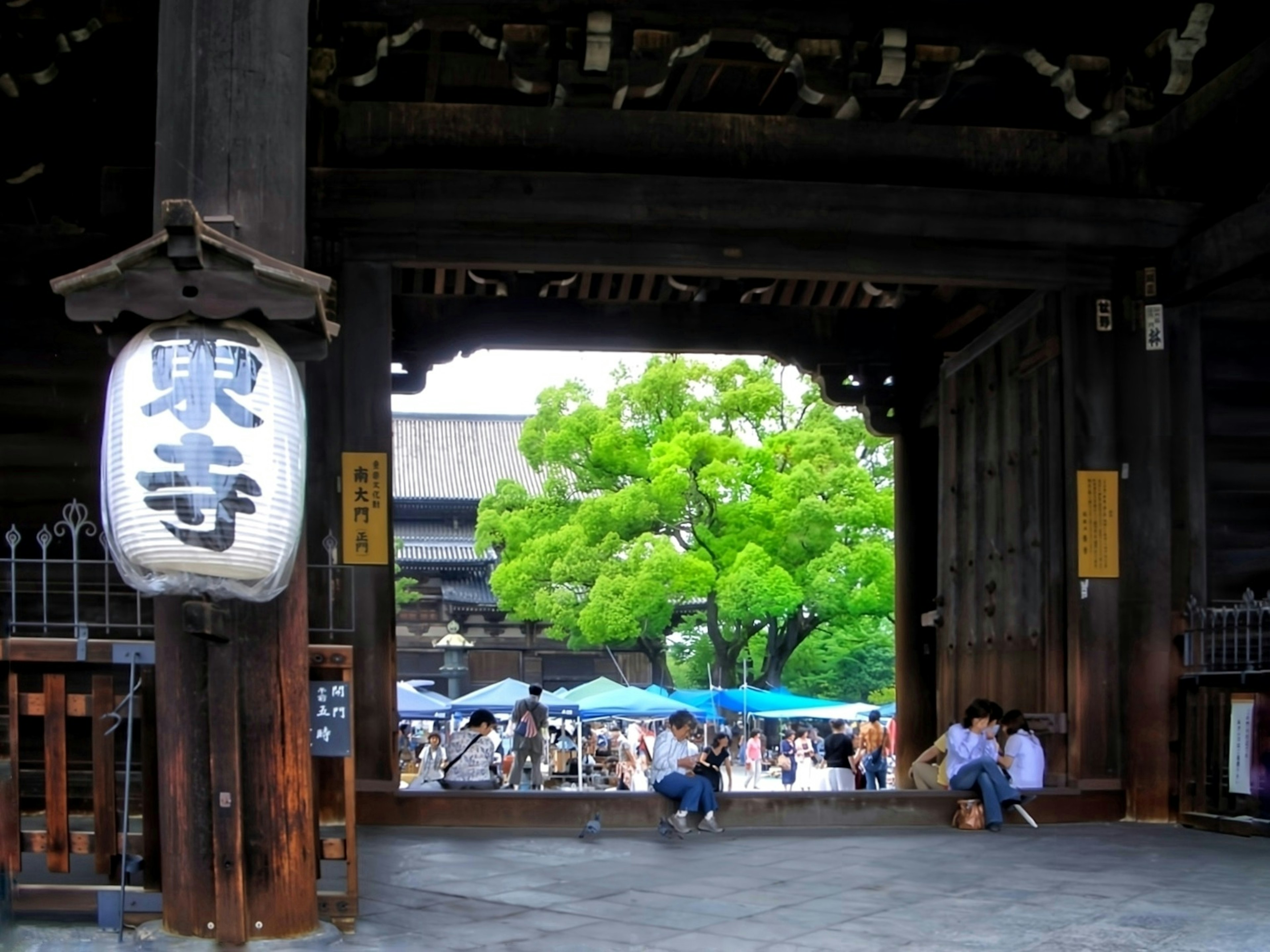 大きな木と賑やかな人々が見える寺院の門の内部