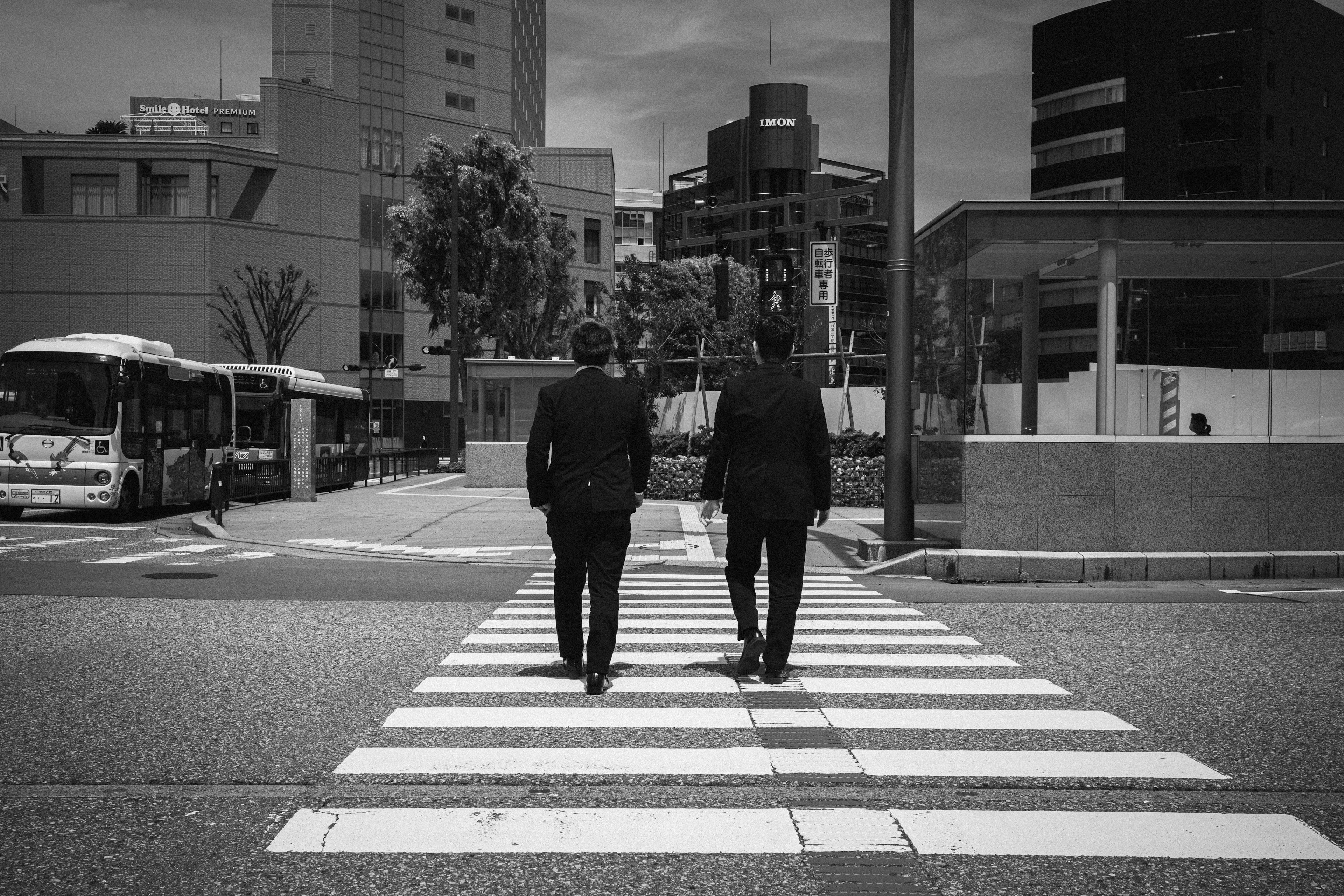 Dos hombres caminando por un paso de peatones en una escena urbana en blanco y negro