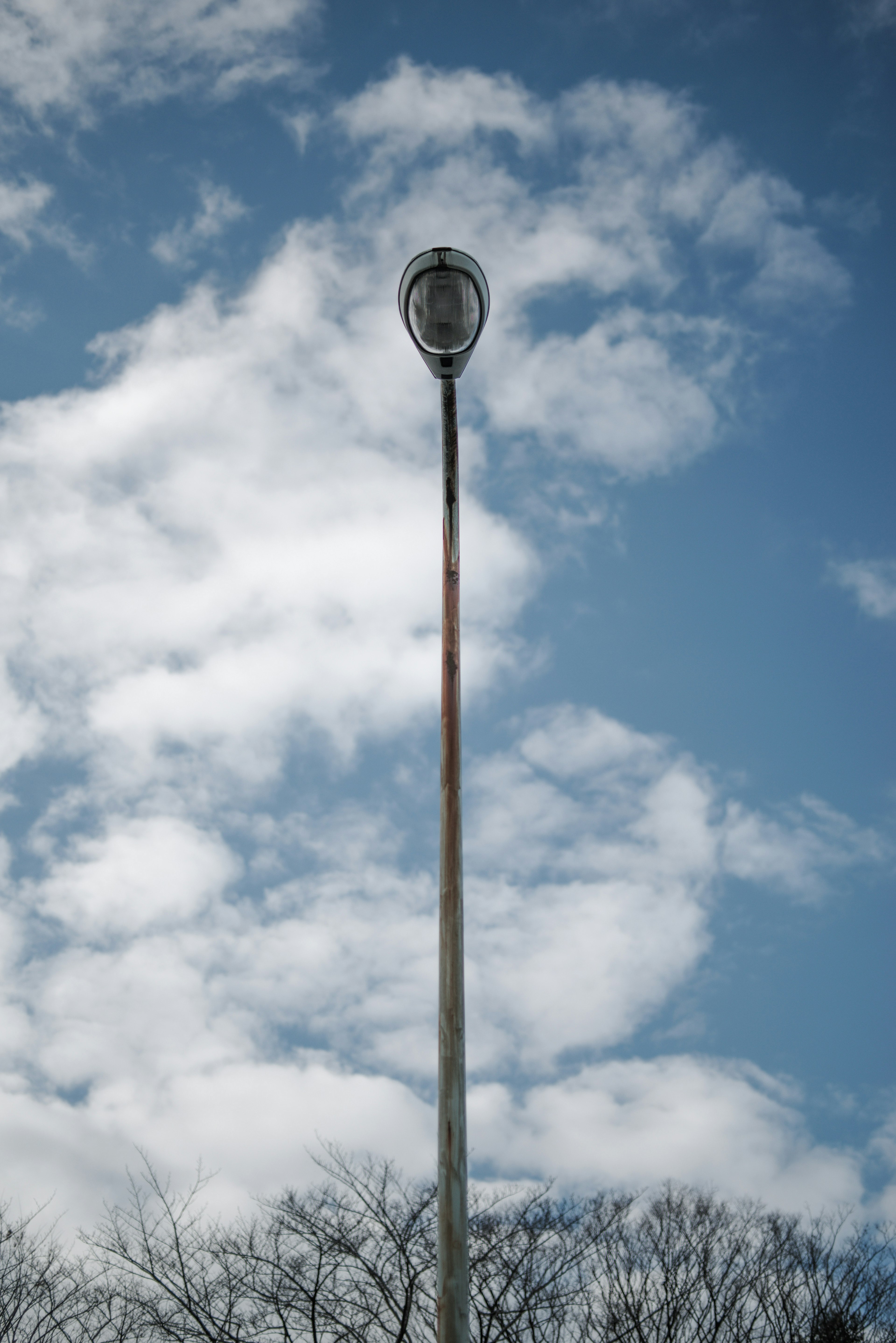 Lampadaire haut sous un ciel bleu avec des nuages blancs