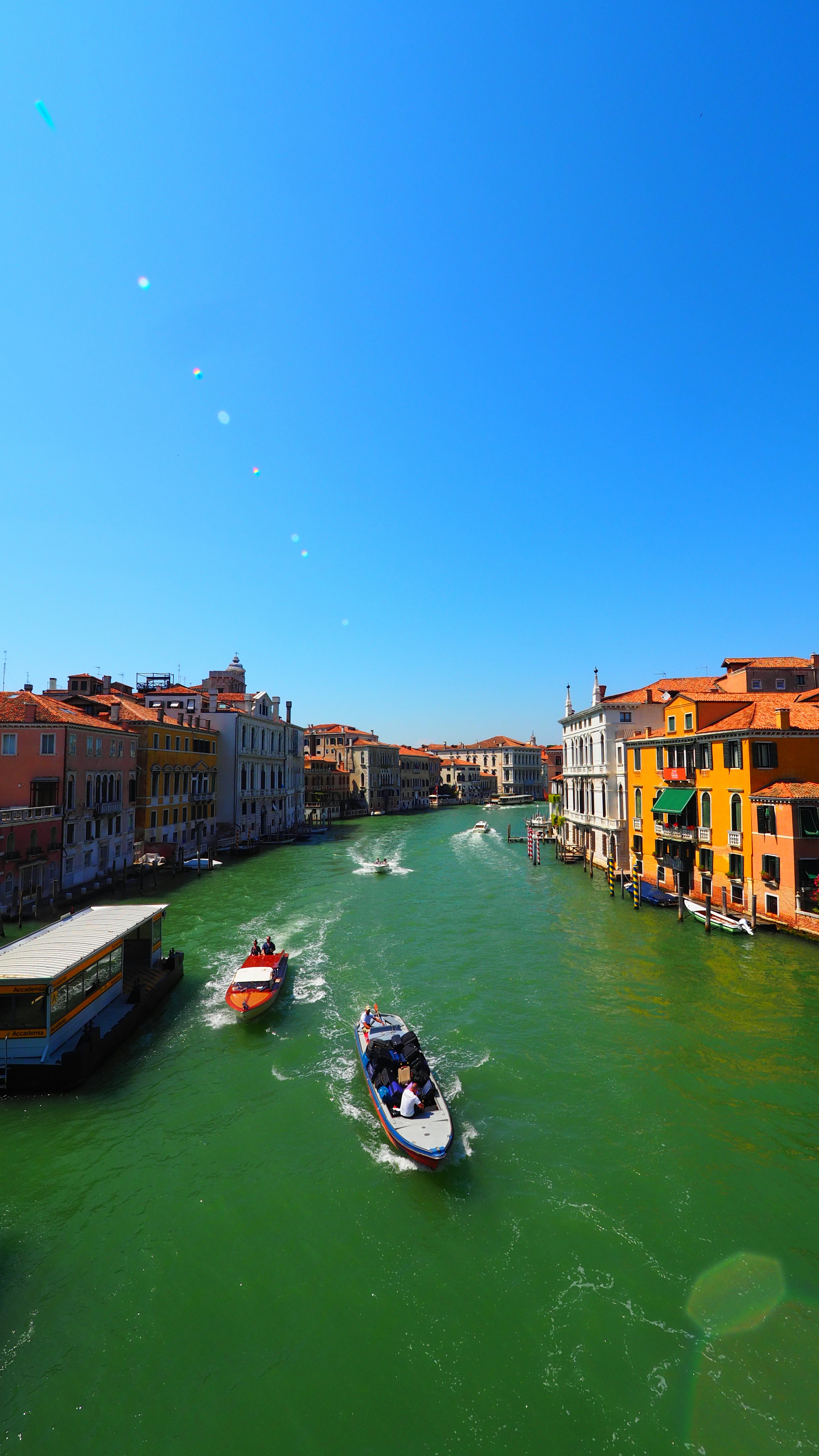 View of boats navigating a green canal under a clear blue sky