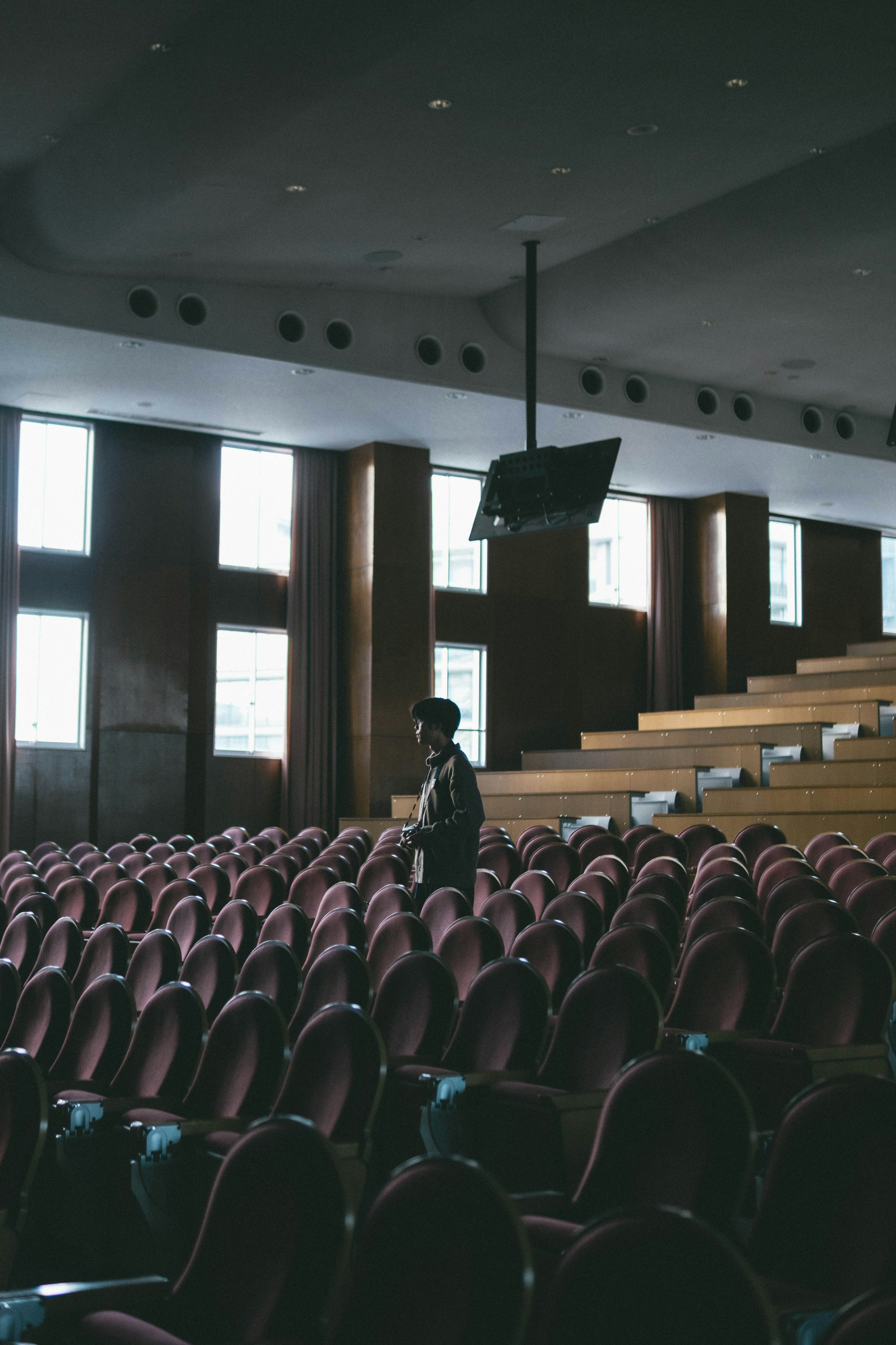 Une personne se tenant dans un auditorium faiblement éclairé avec des rangées de sièges rouges