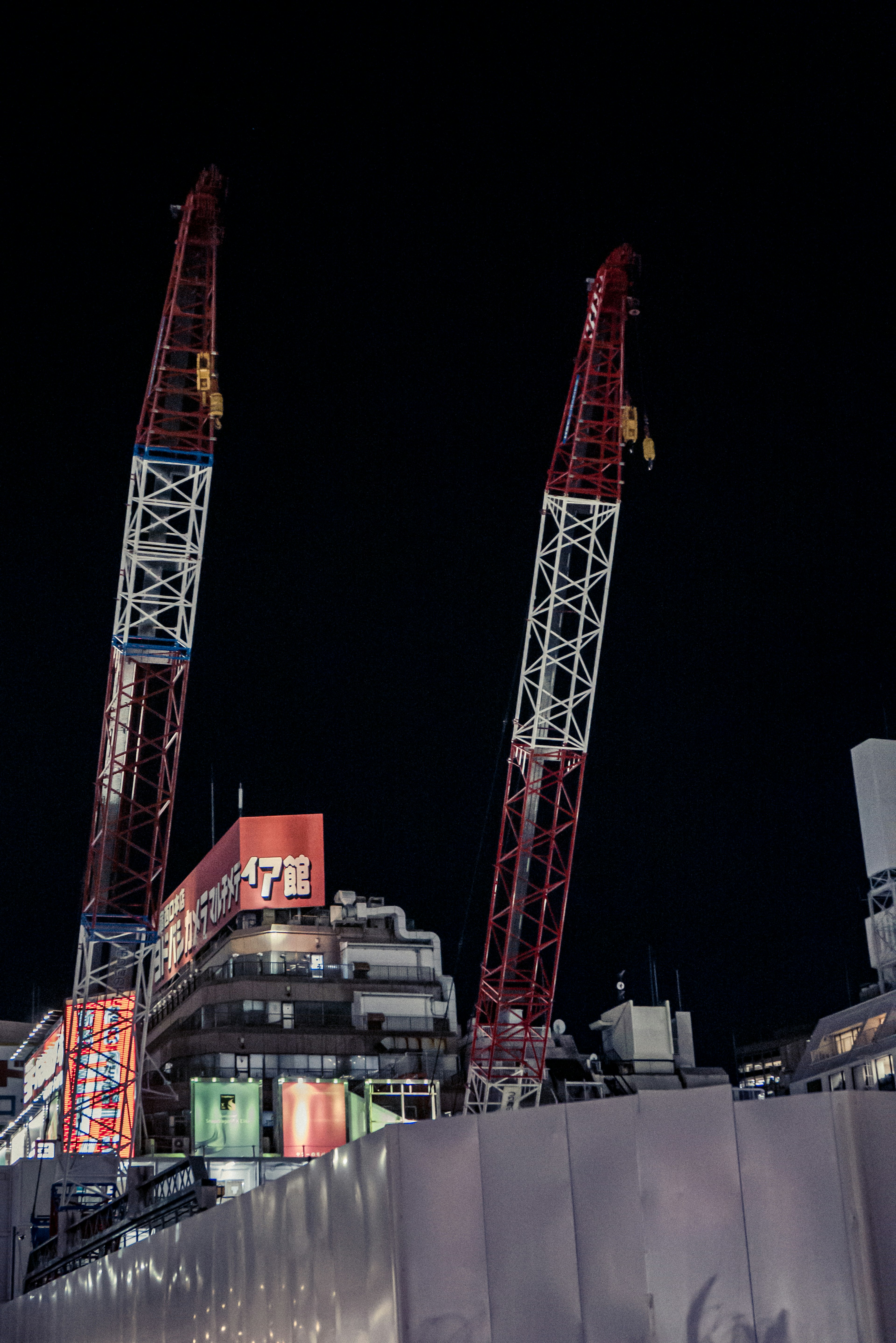 Two red and white cranes standing in a night cityscape