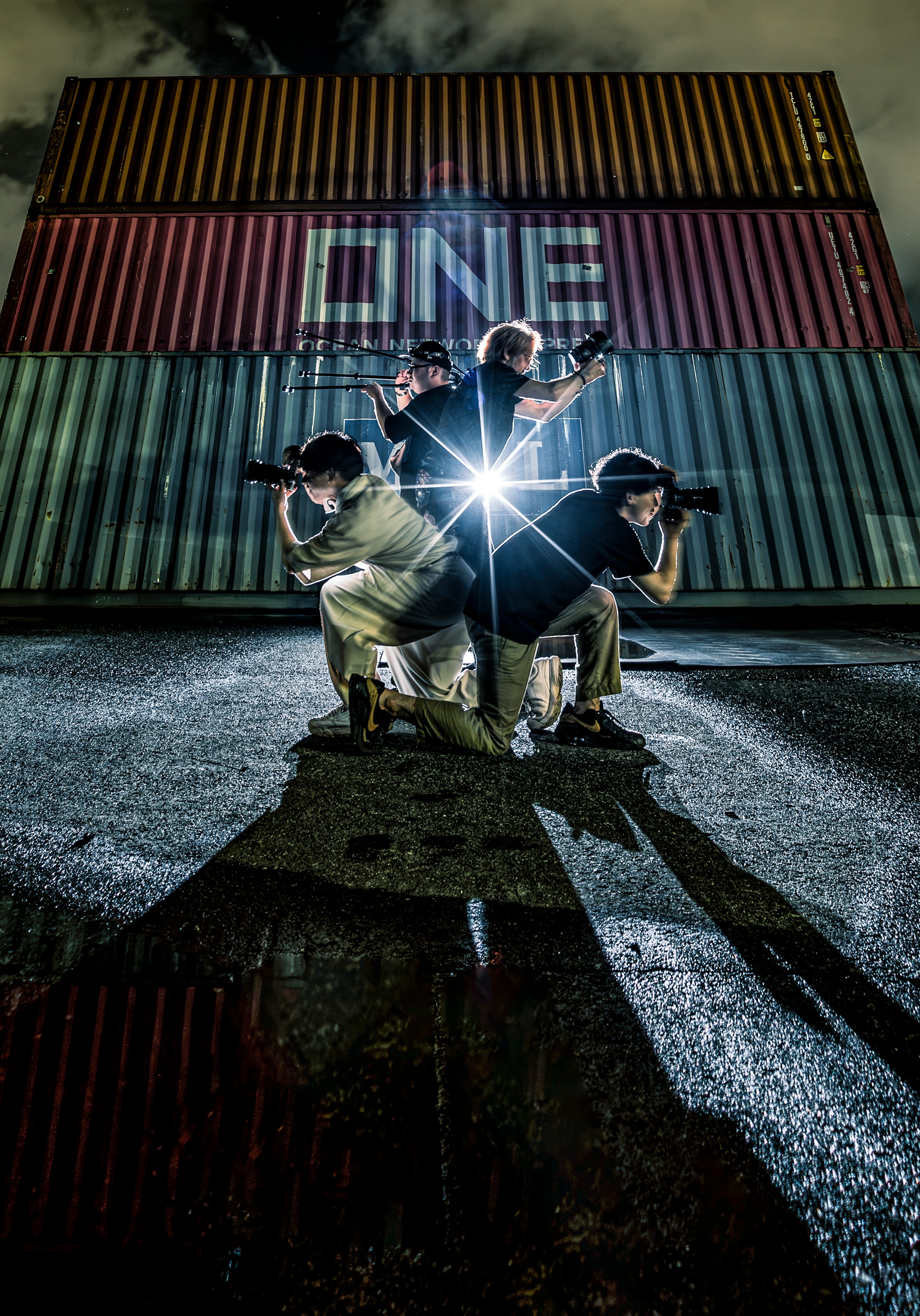 Four individuals posing with lights against a backdrop of shipping containers