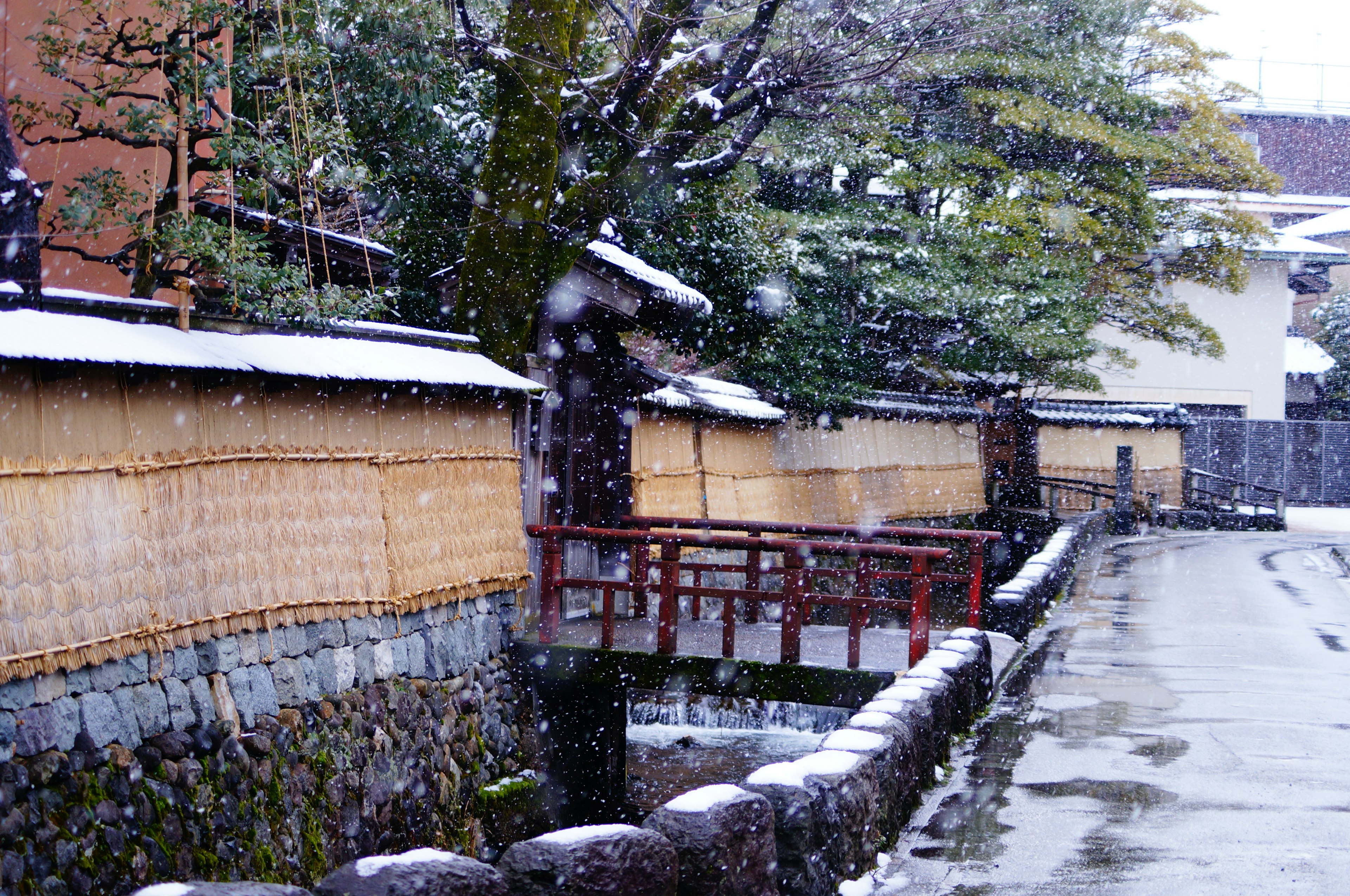 Snowy landscape featuring a quiet street and a red bridge