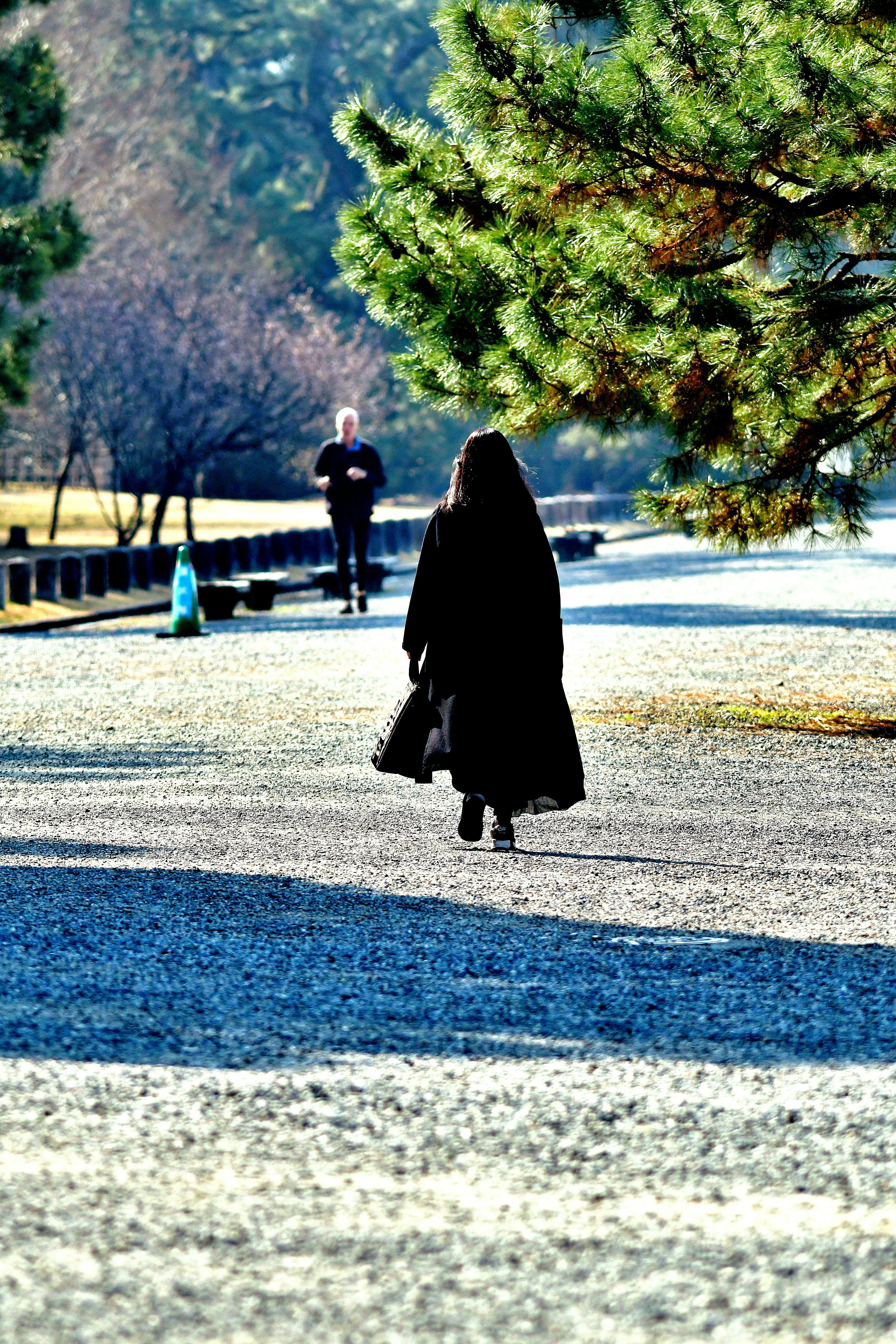 Una donna in un cappotto nero che cammina su un sentiero del parco con un uomo sullo sfondo