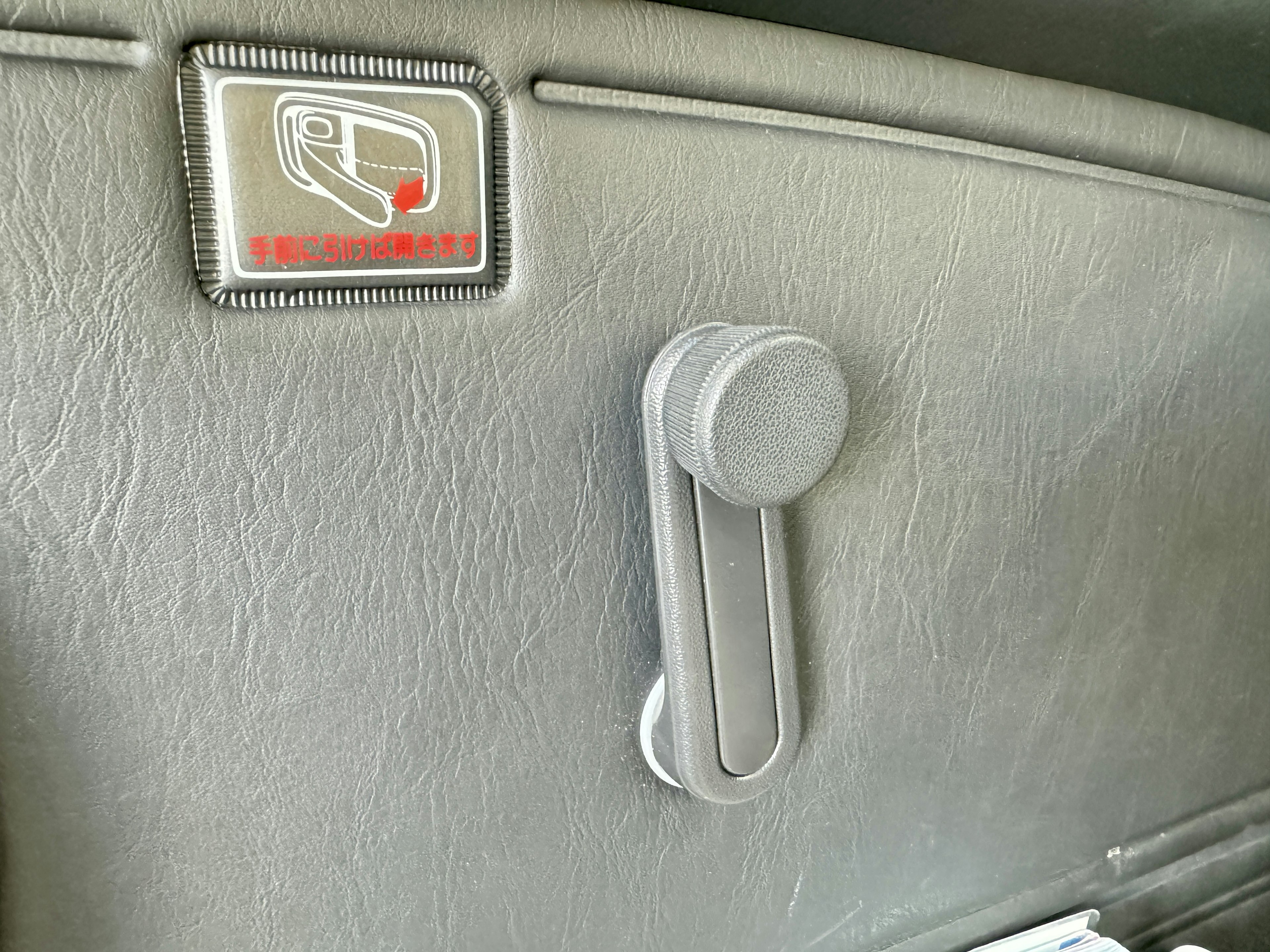 Imagen de un panel de plástico gris y una palanca de ajuste de asiento en el interior de una puerta de automóvil