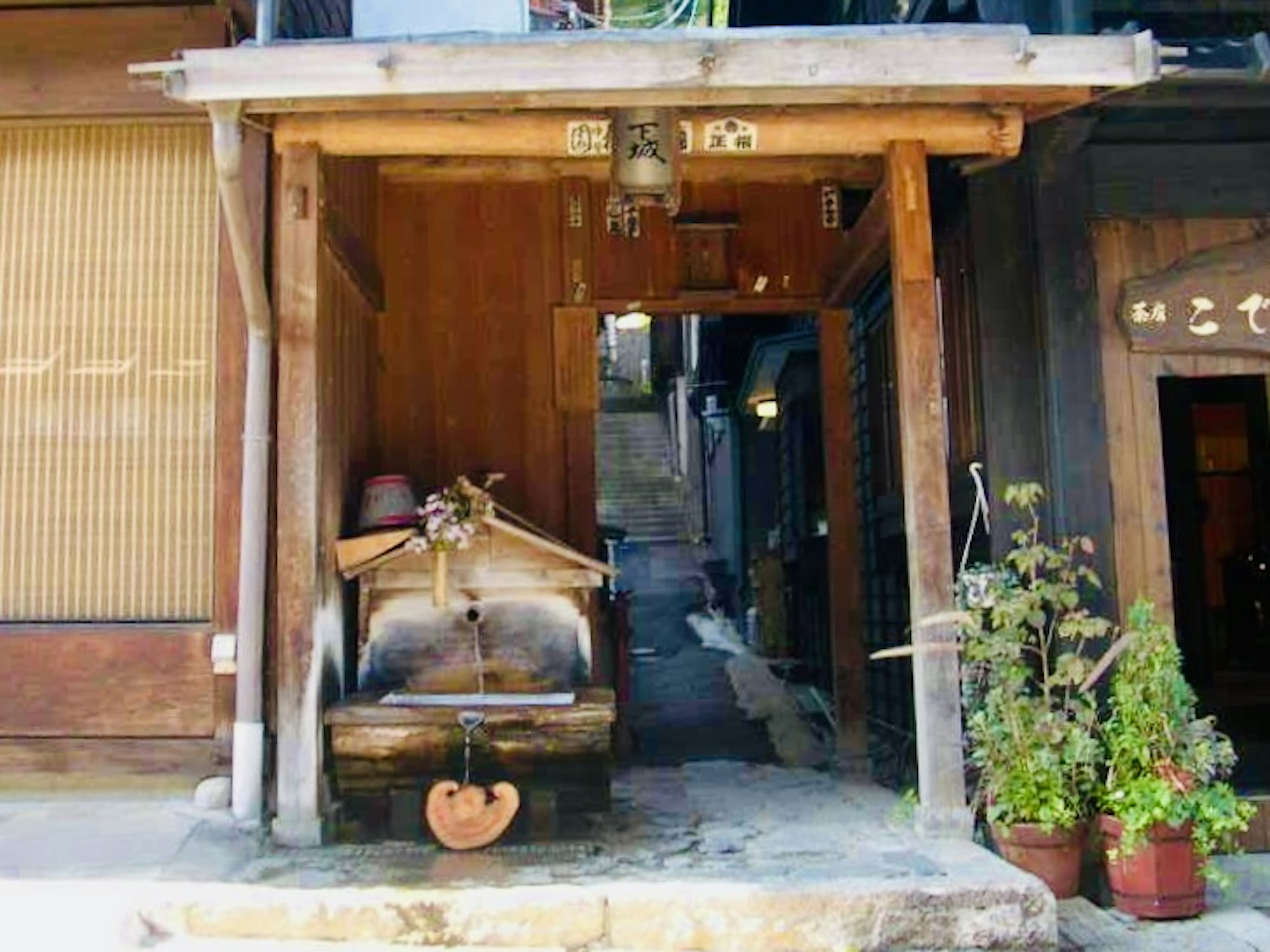 Entrada de una estructura de madera con una rueda de agua y plantas en macetas