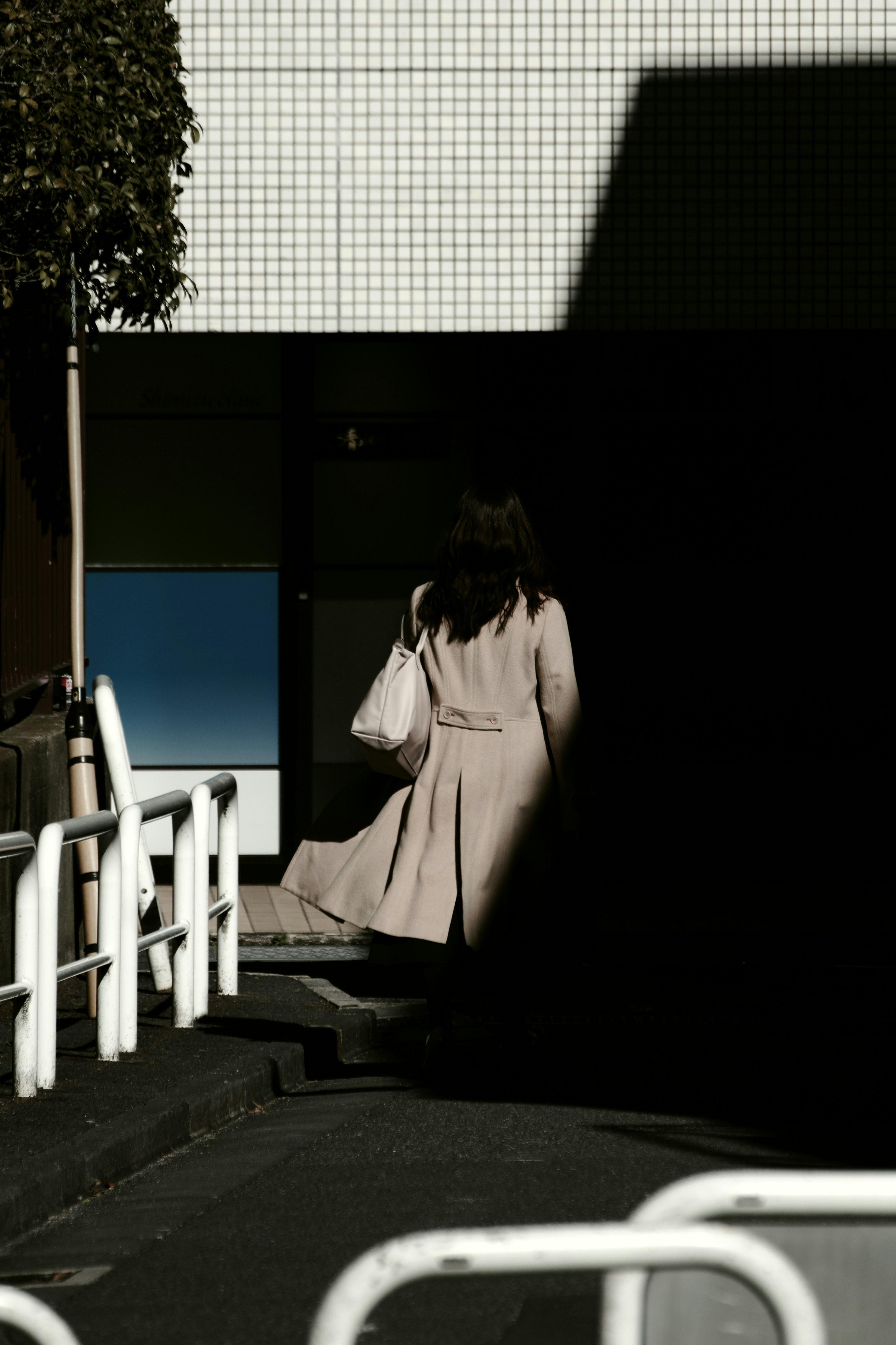 A woman in a beige coat walking away in a city setting