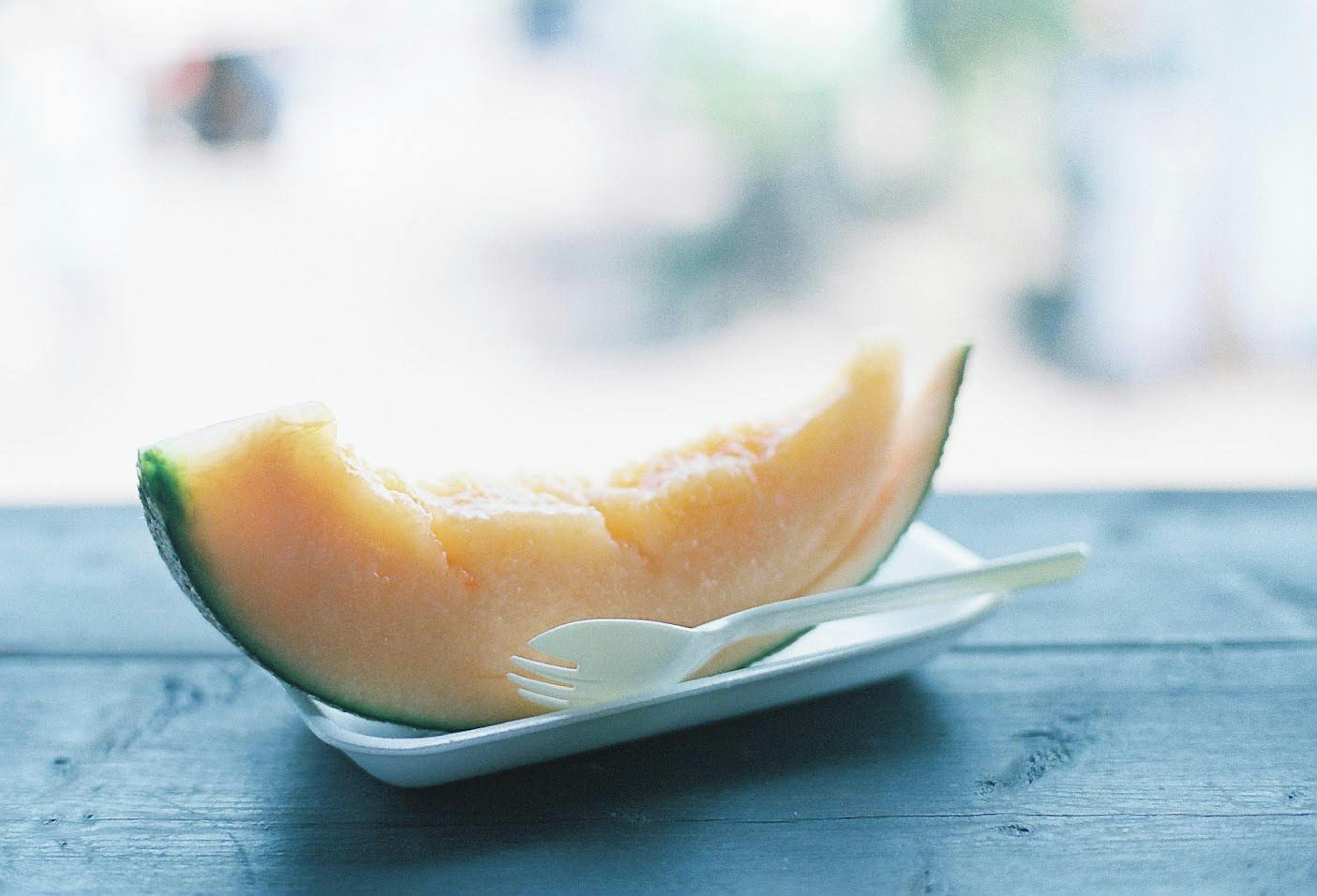 A slice of melon on a small white plate with a spoon